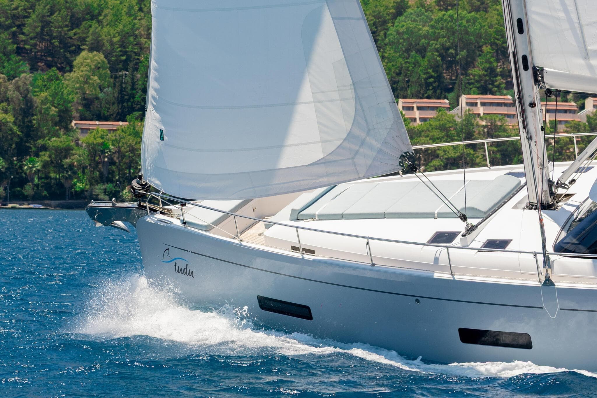 Sailing yacht Moody 48 Deck Salon 2026 cruising on blue waters near lush coastline.