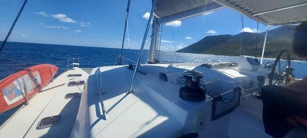 Lagoon 440 catamaran sailing on open sea, sunny day, mountainous coastline in background.