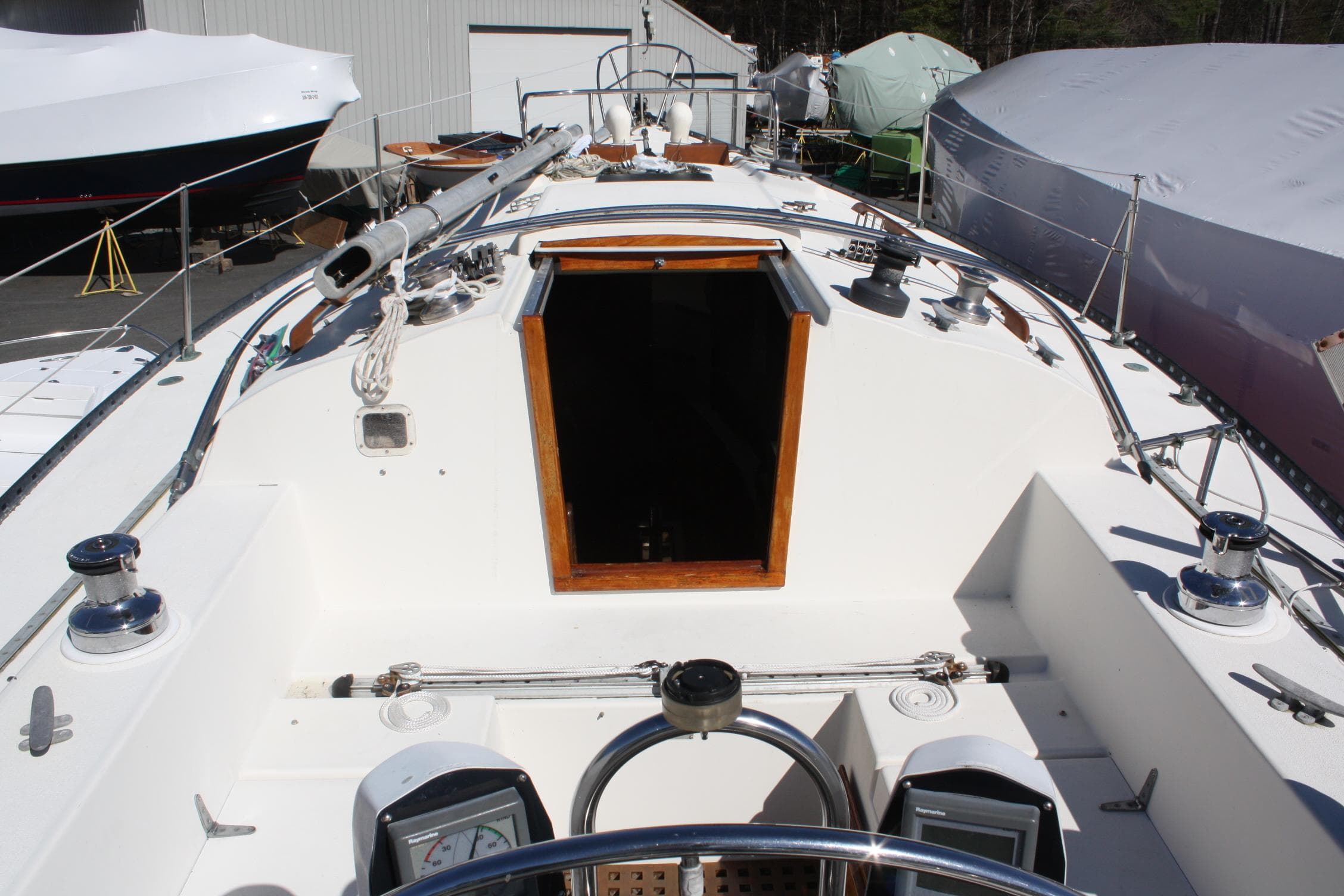 1976 C&C 38 sailboat deck with open hatch, docked in a boatyard.