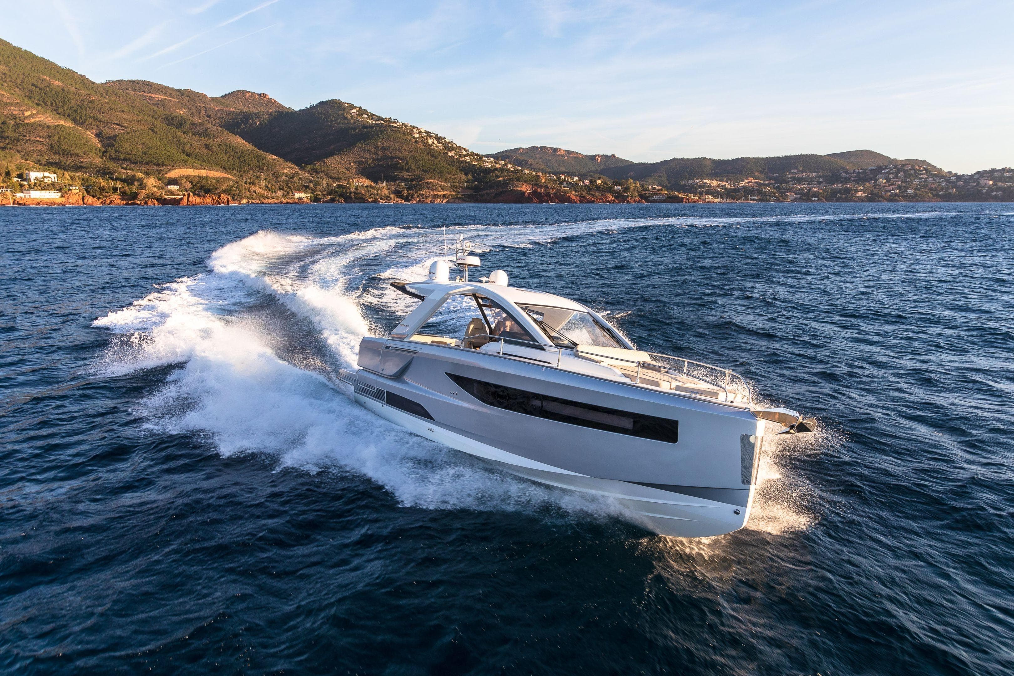 2026 Jeanneau DB/37 IB yacht cruising on open water with scenic mountain backdrop.
