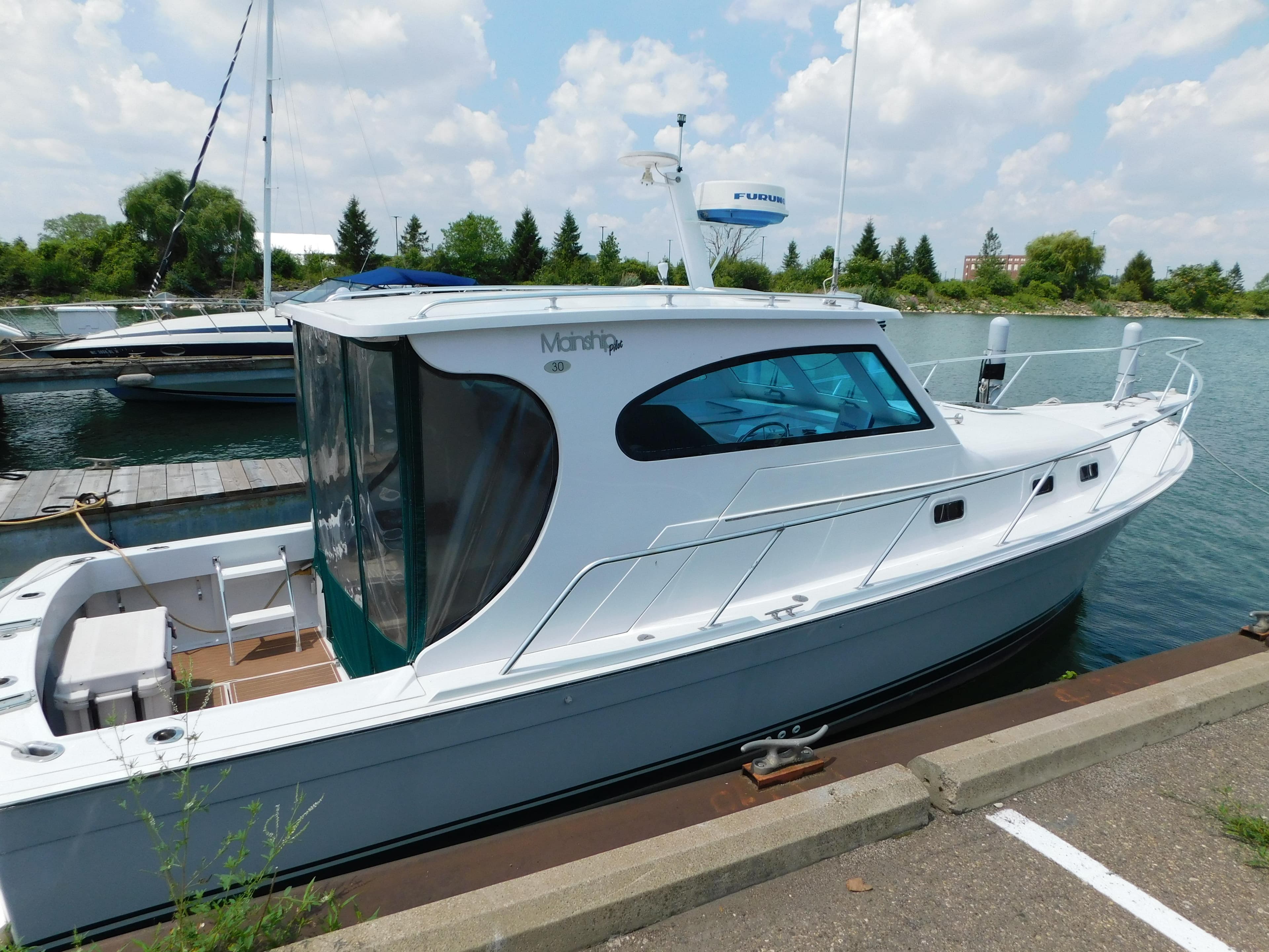 1999 Mainship Pilot 30 docked by a serene waterfront under a partly cloudy sky.