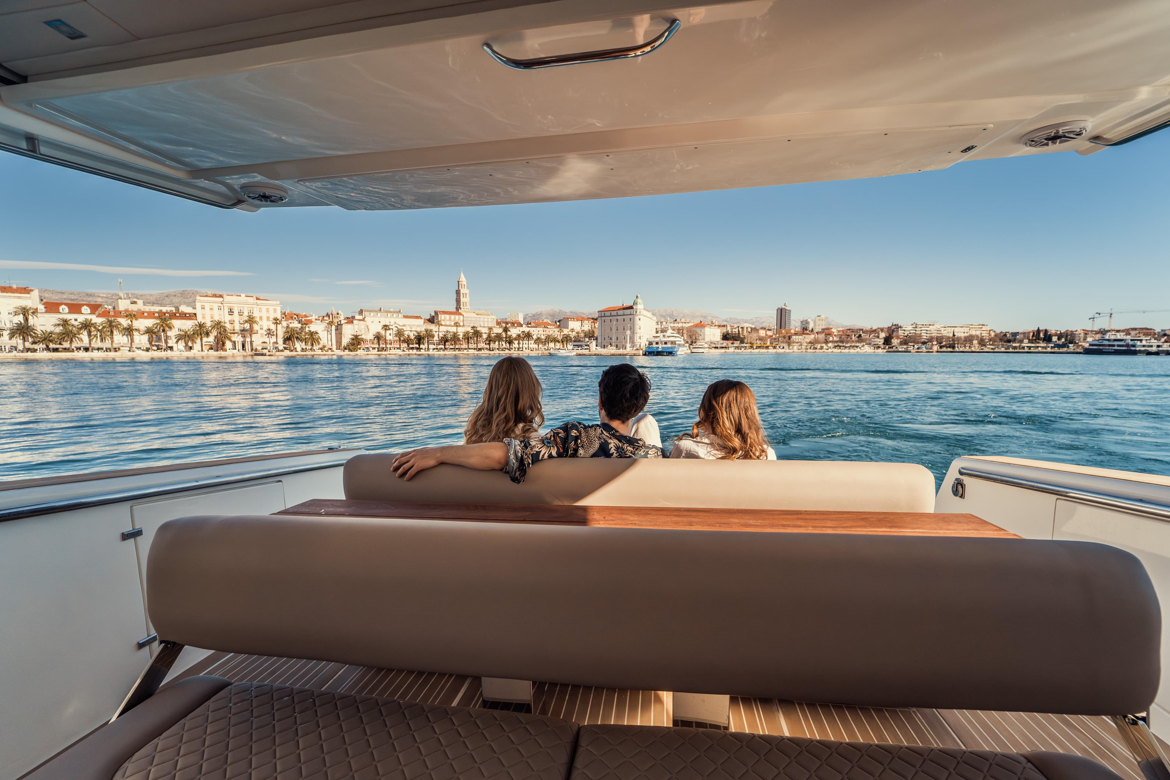Three people relaxing on a Makai M37 yacht, enjoying a scenic coastal view.