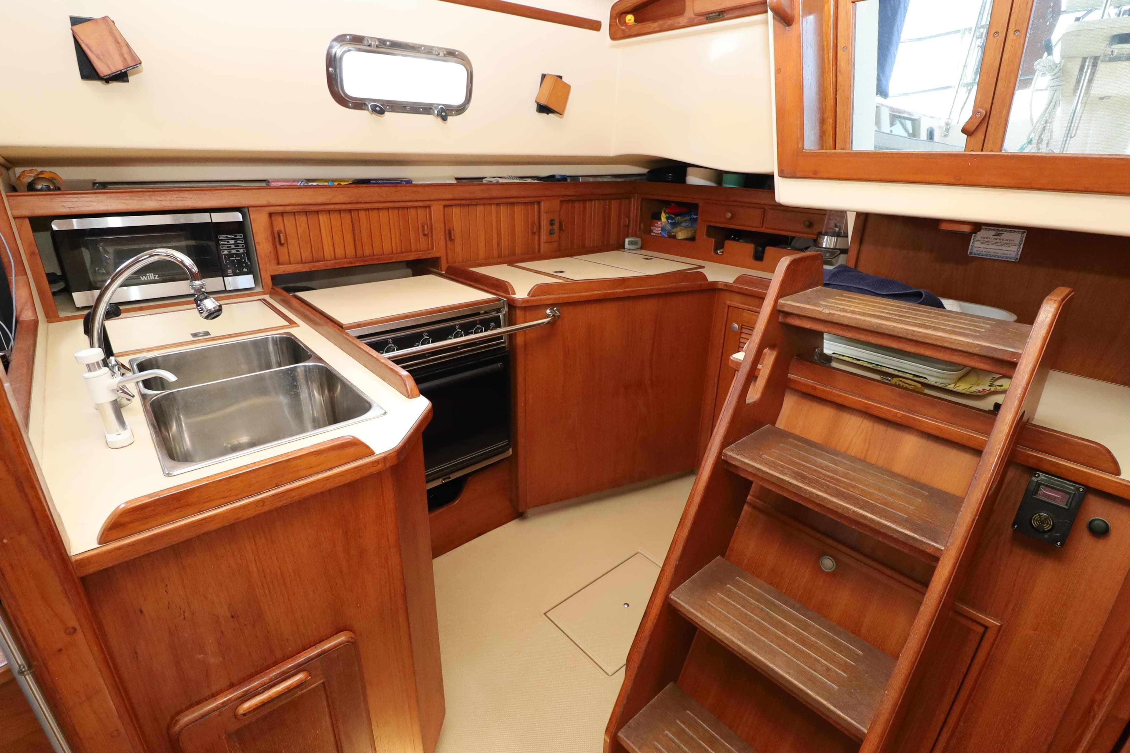 1996 Island Packet 40 yacht kitchen with wooden cabinetry, sink, stove, and microwave.