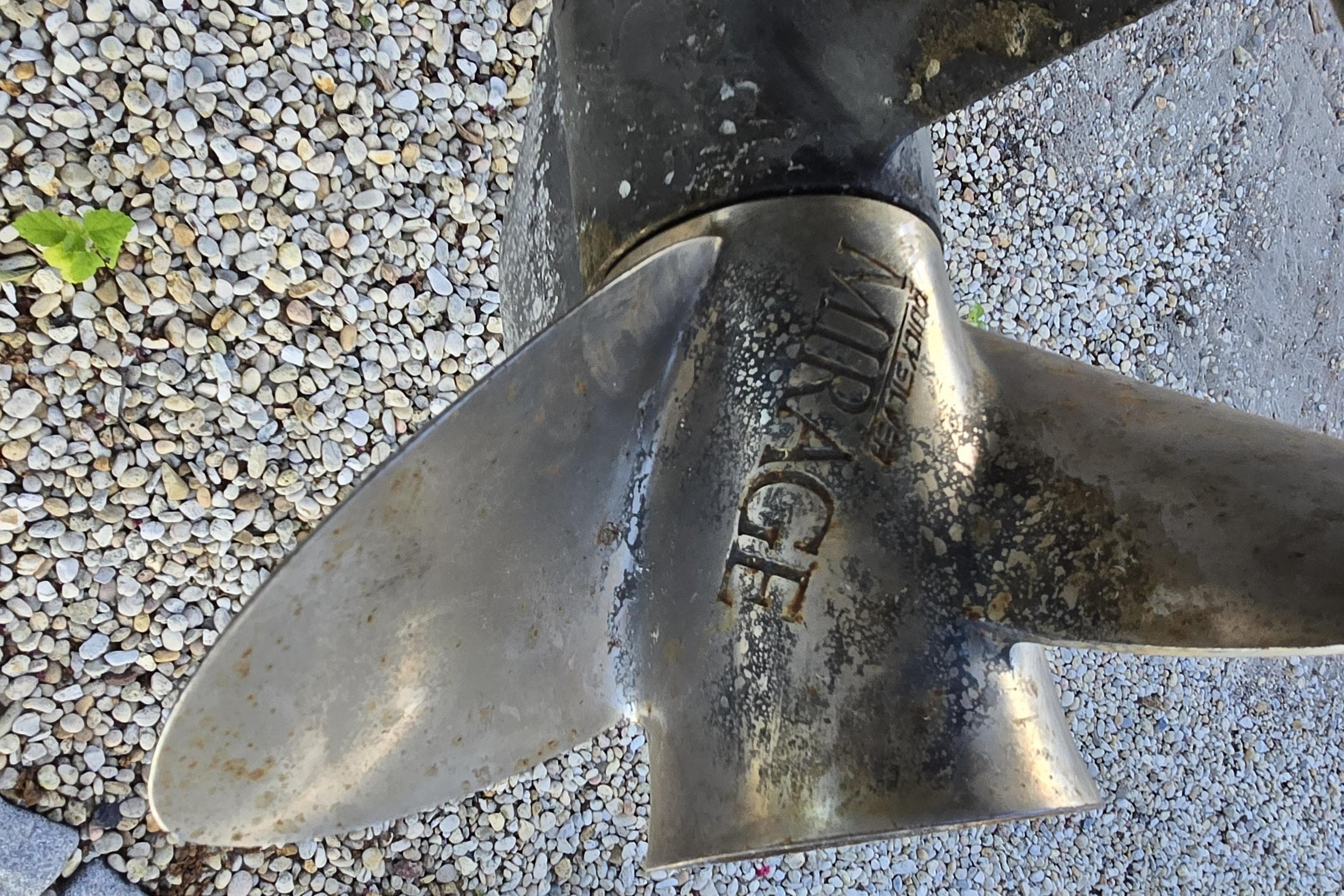 Close-up of a weathered boat propeller on gravel, featuring "Mirage" branding.