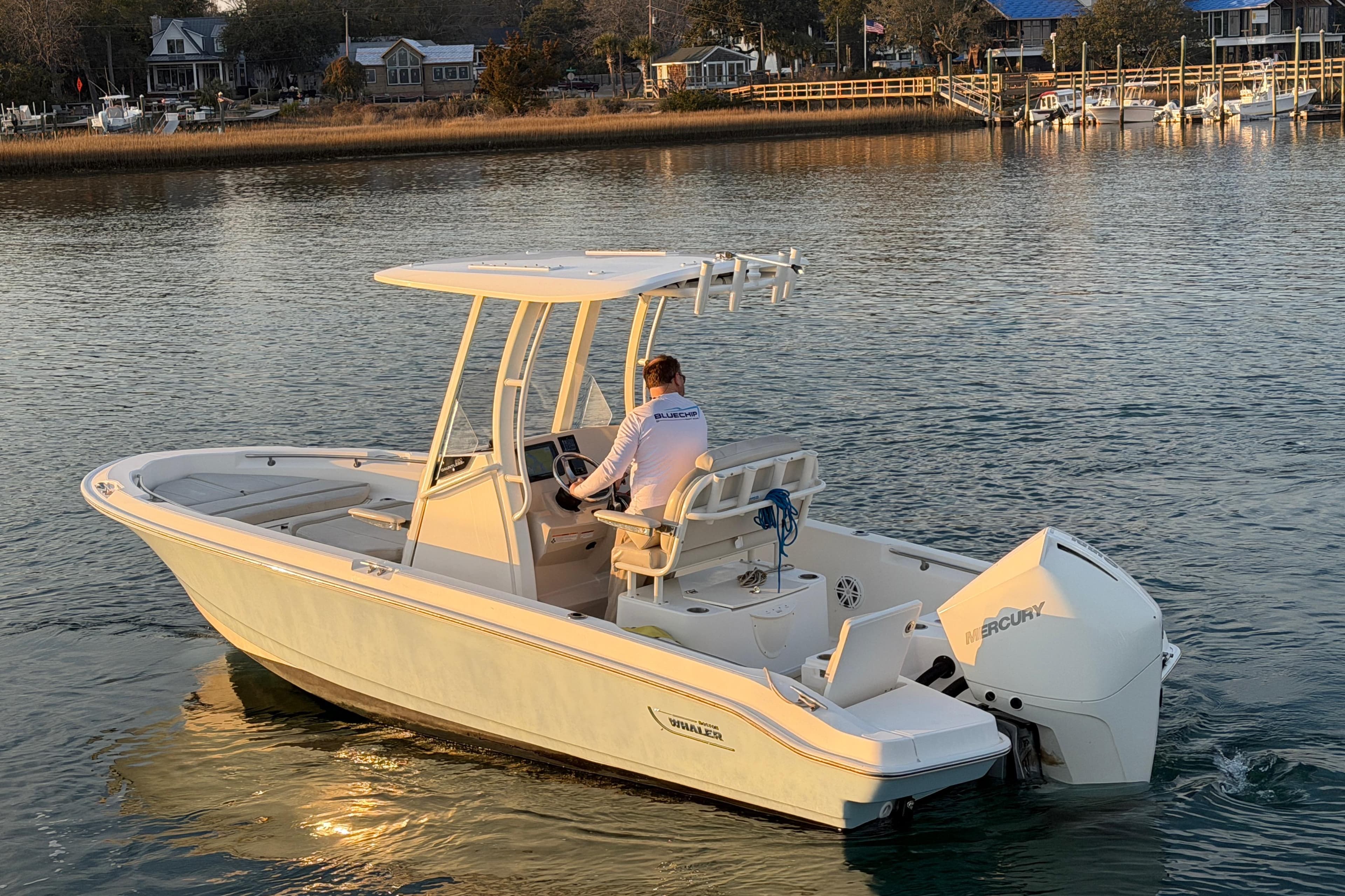 2023 Boston Whaler 220 Dauntless boat cruising on calm water near a shoreline.