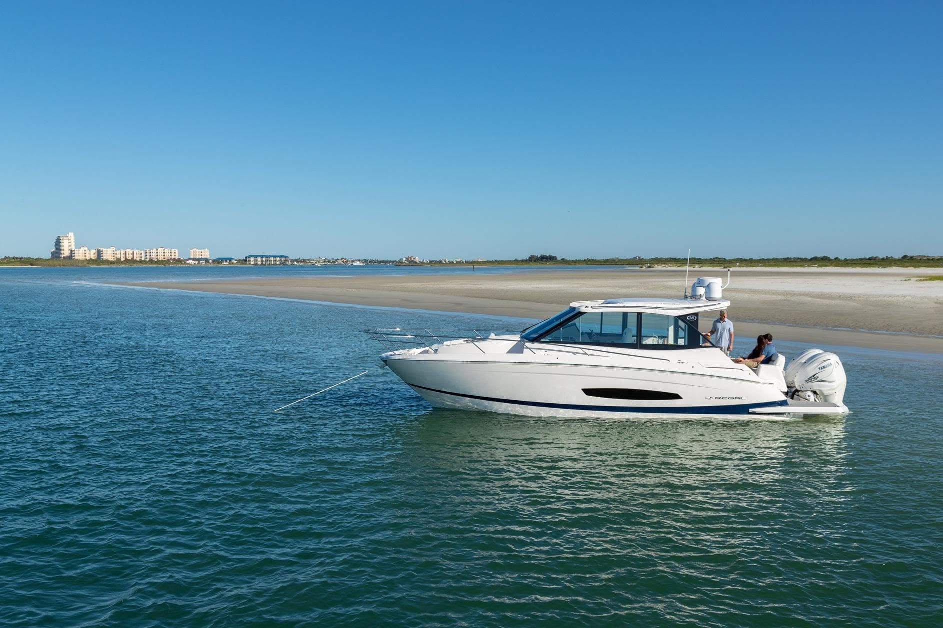 2026 Regal 36 XO boat cruising near a sandy shoreline under a clear blue sky.