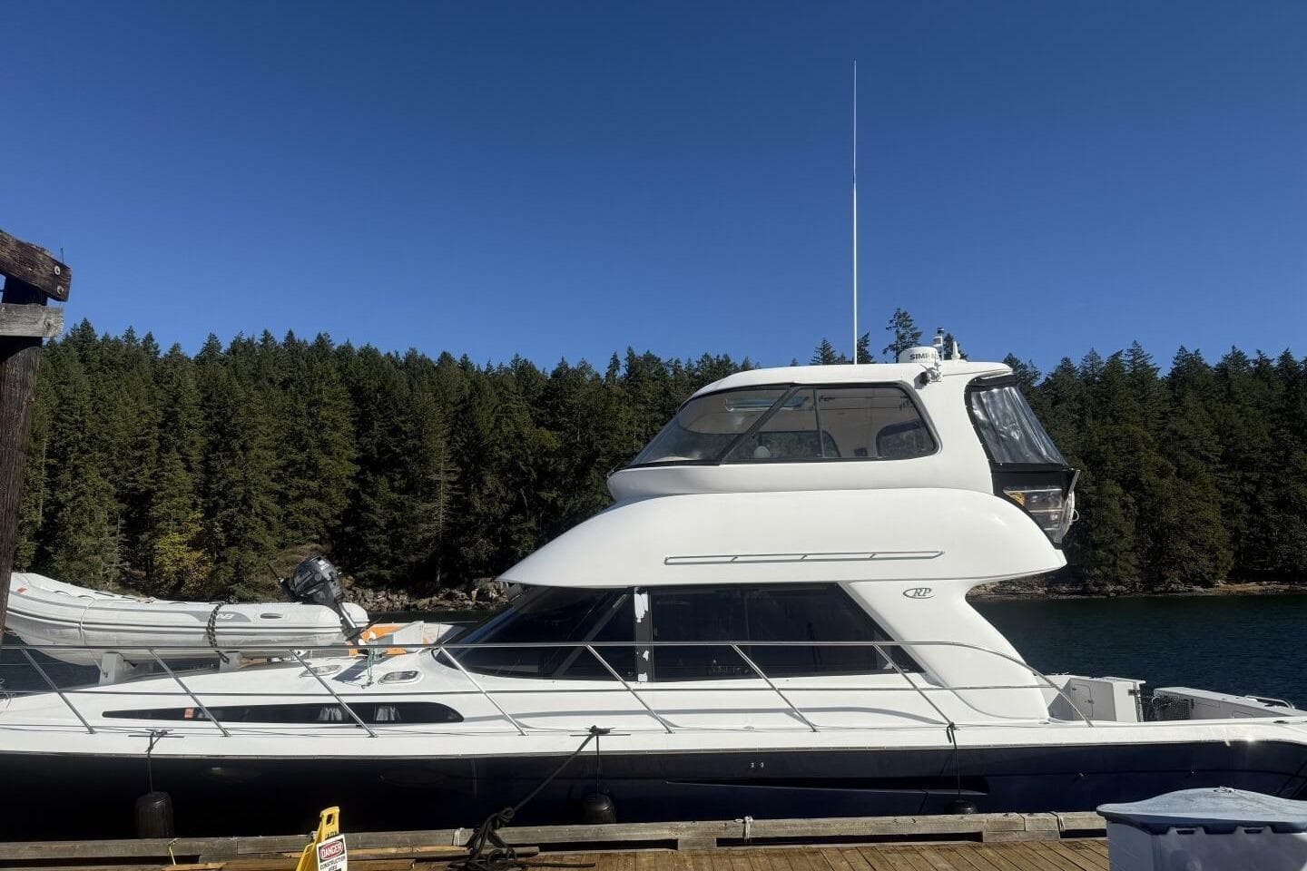 2000 Royal Pacific 476 Sport Cruiser docked by forested shoreline under clear blue sky.