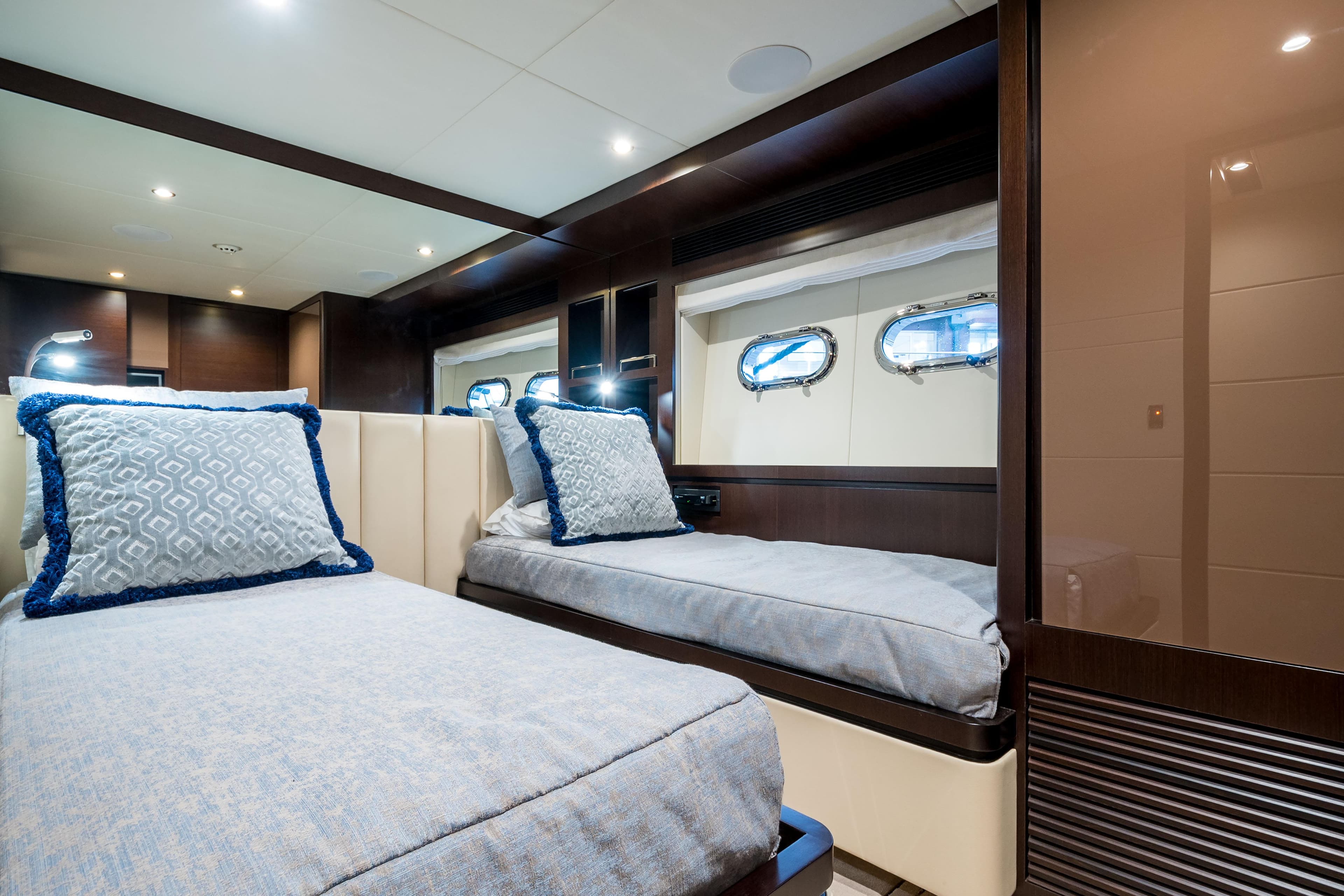 Luxurious twin cabin interior on 2020 Horizon RP100 yacht, featuring elegant bedding and porthole windows.