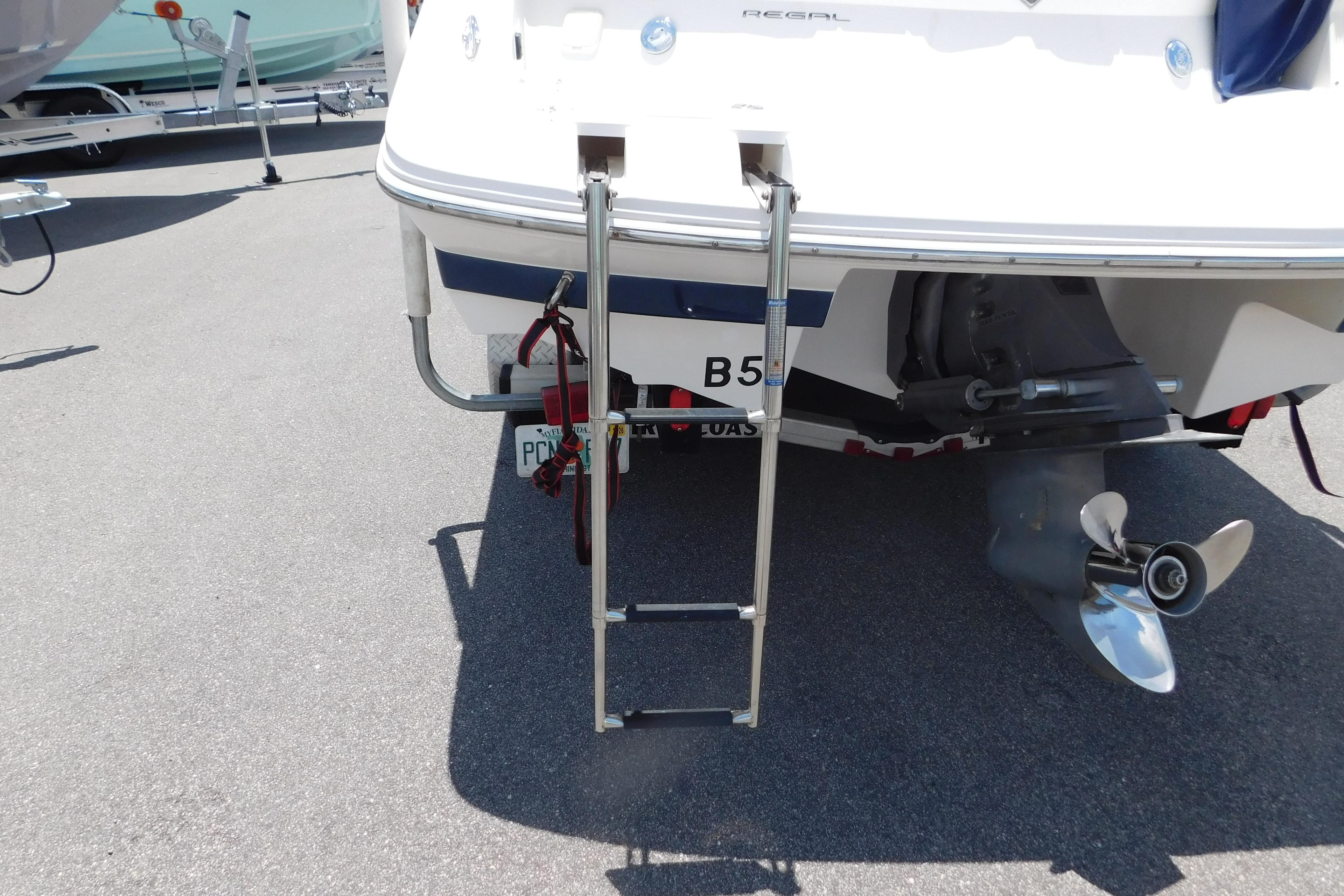 2004 Regal 2250 LSC boat with ladder and propeller, parked on asphalt.