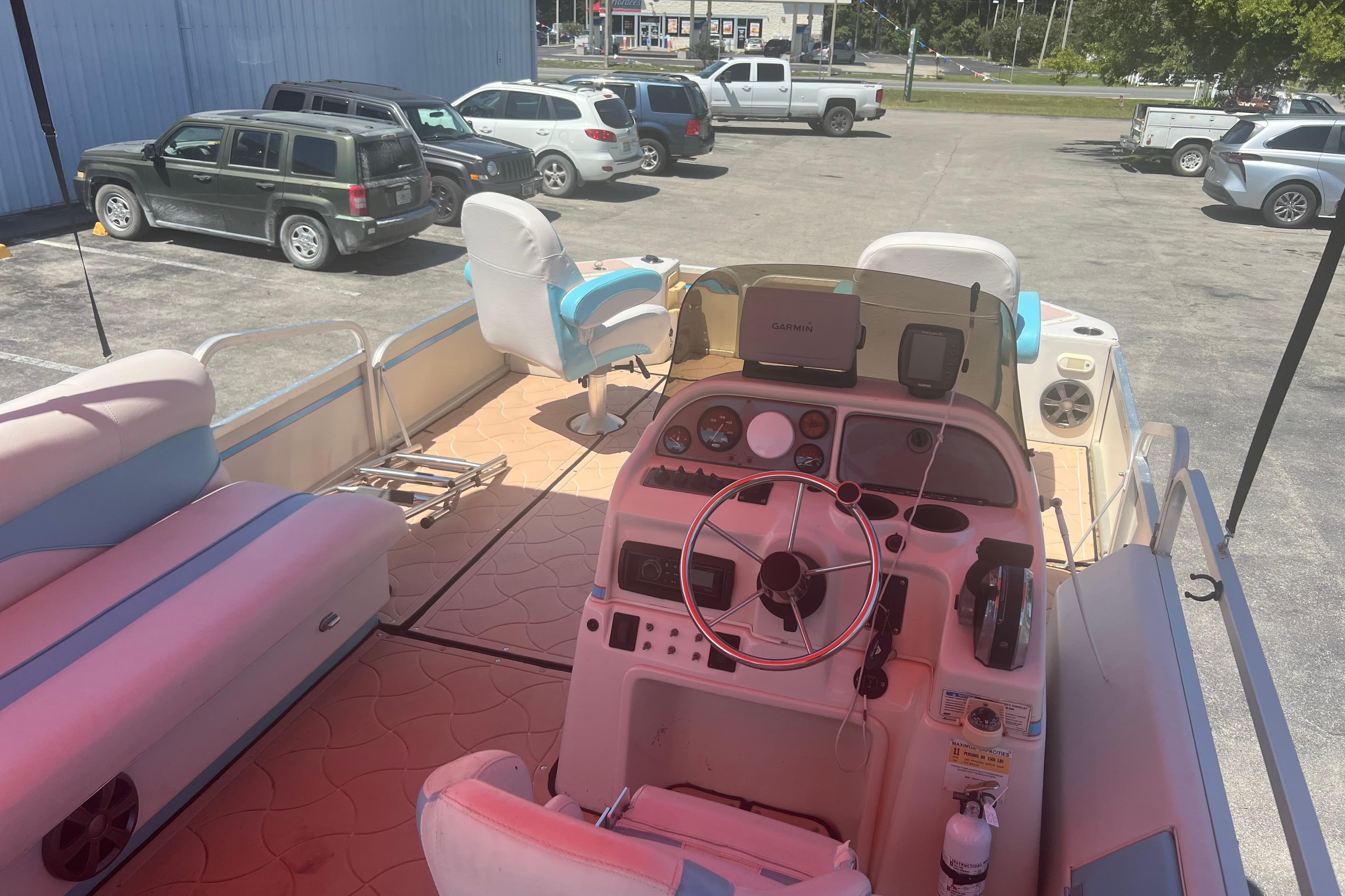 2005 G3 LX20 boat interior with steering wheel, seats, and parked cars in background.