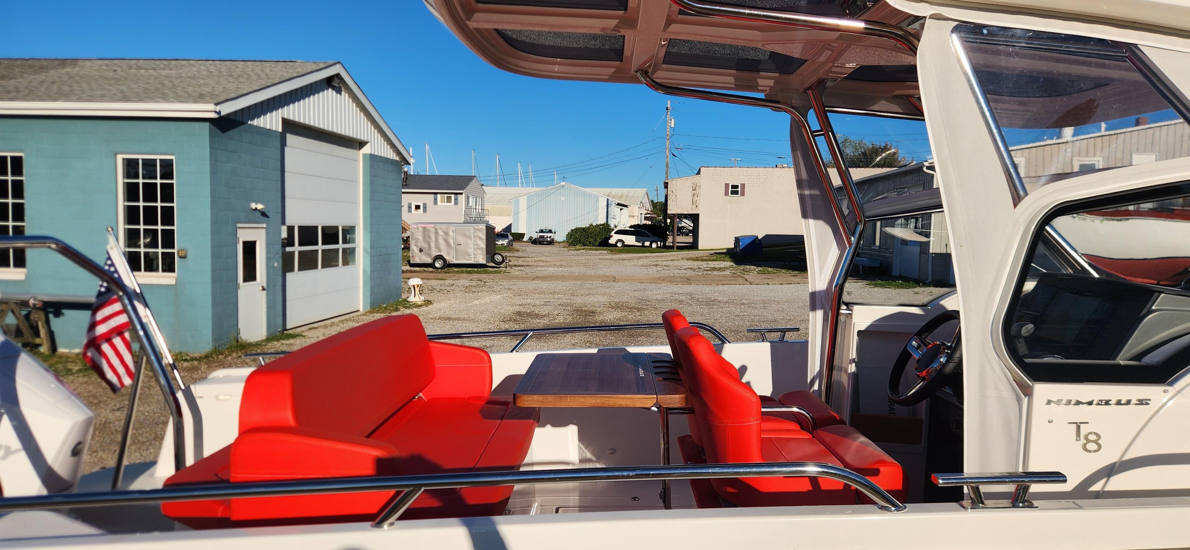 2023 Nimbus T8 boat with red seating and open deck, docked near blue building.