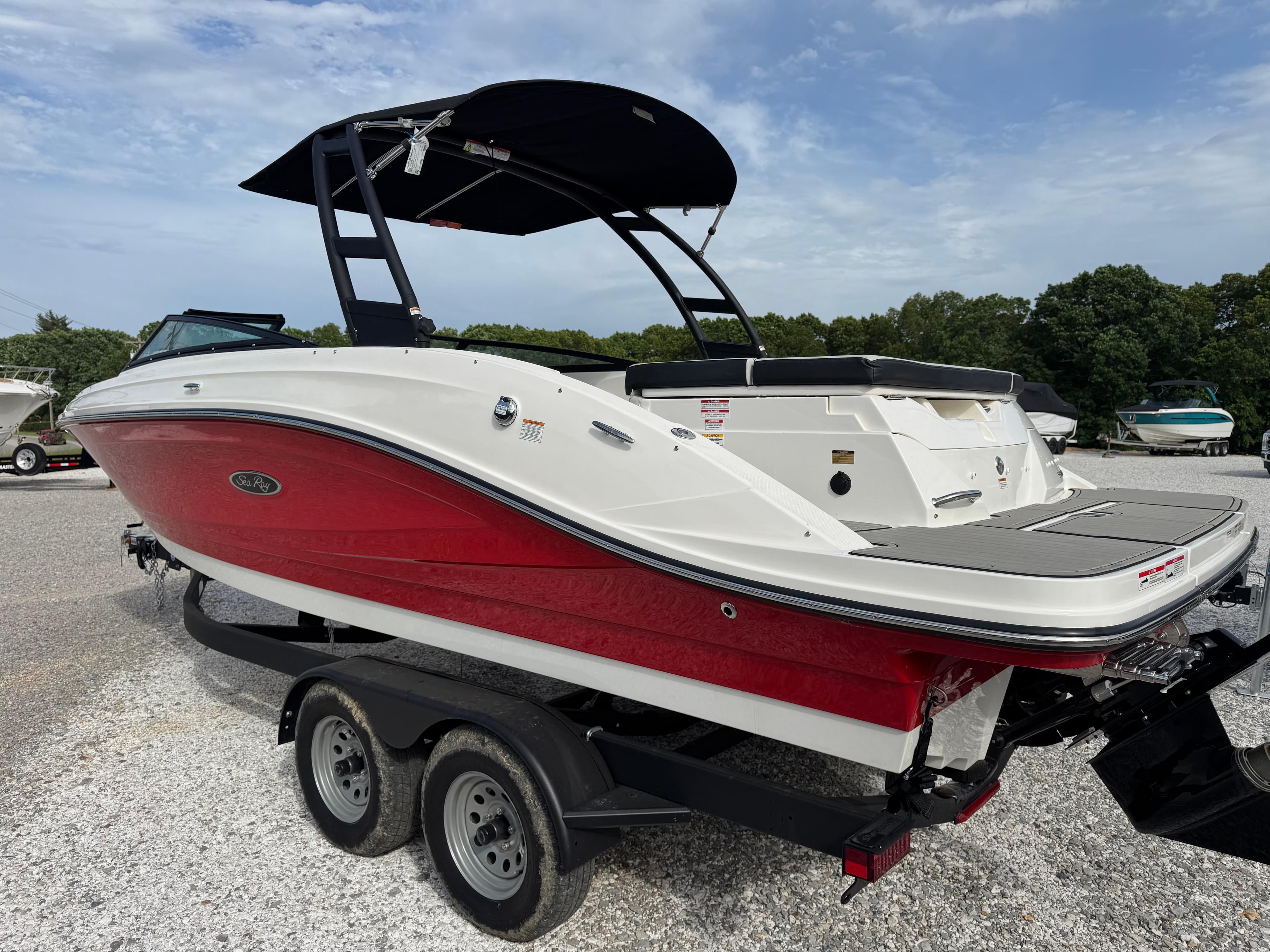 2025 Sea Ray SPX 230 boat with red and white hull on a trailer, parked outdoors.