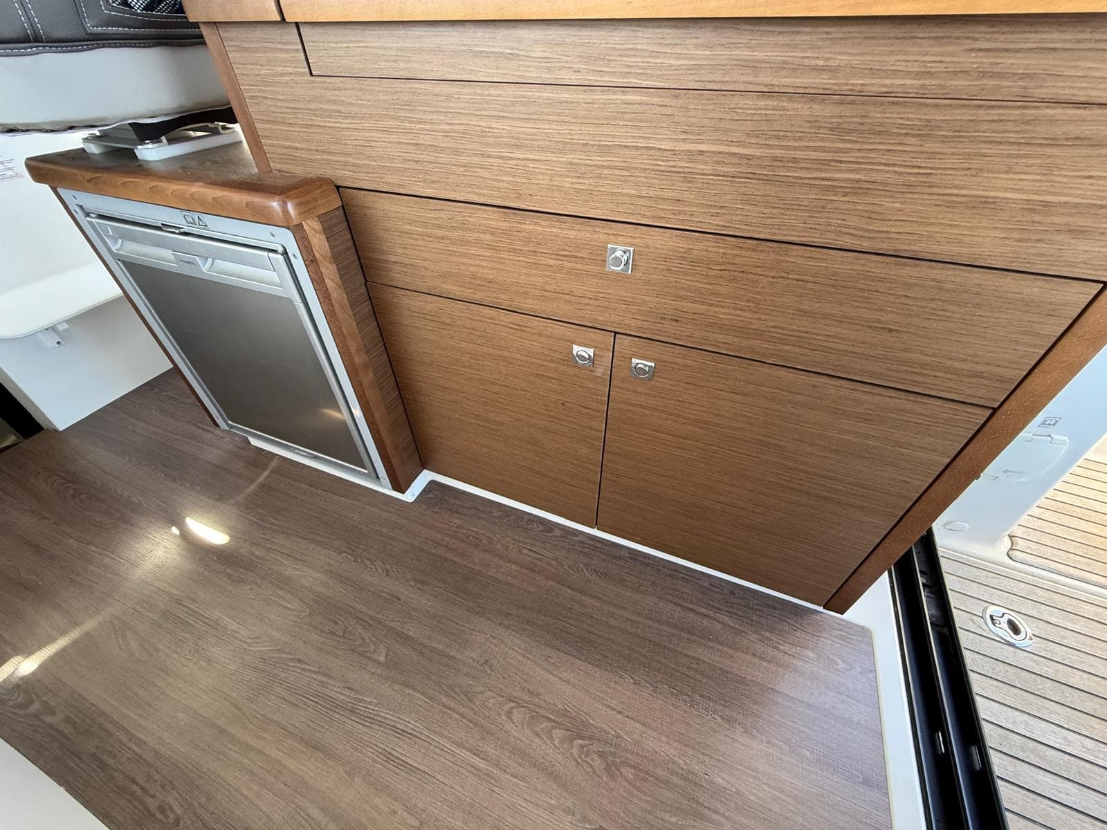 Interior of 2022 Jeanneau Merry Fisher 895, featuring wood cabinetry and compact refrigerator.