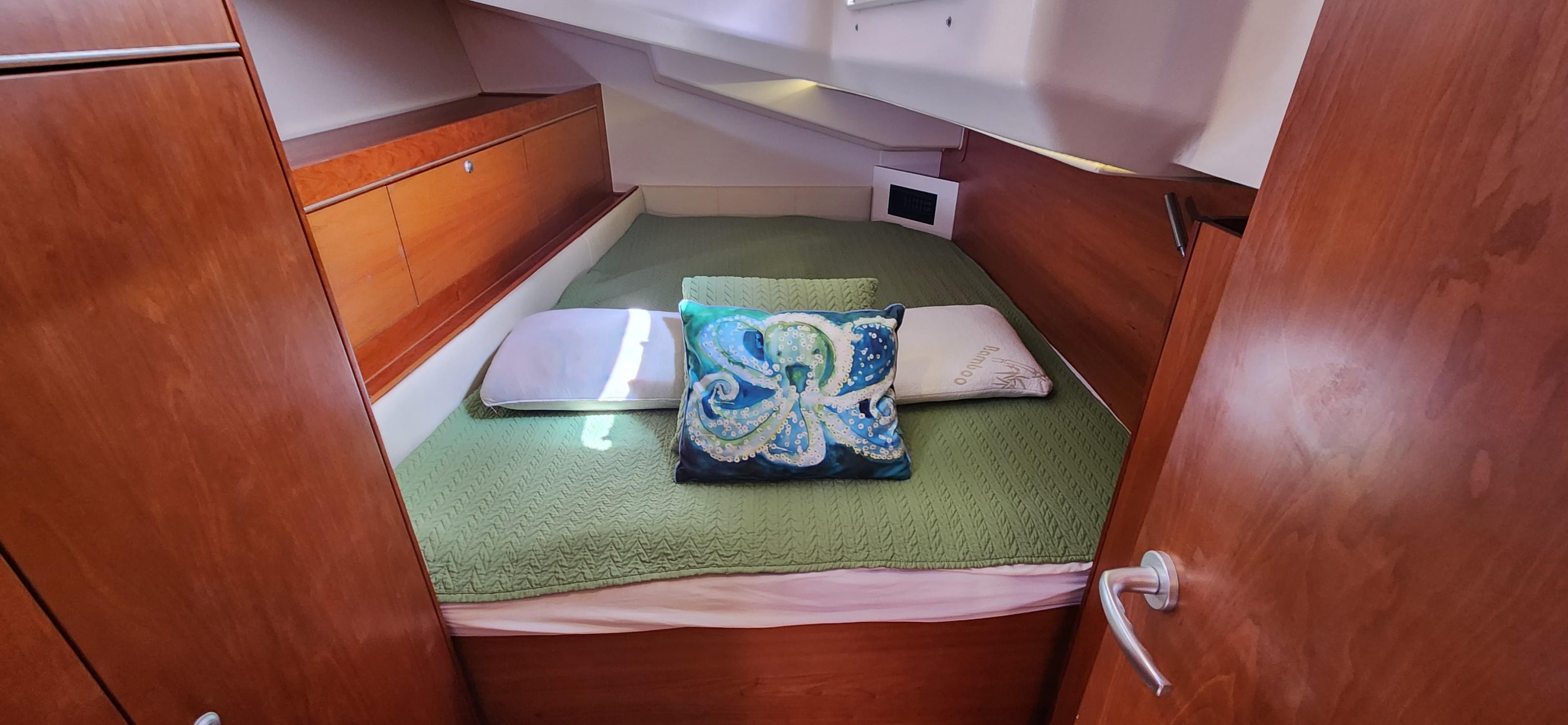 Cozy cabin interior of 2016 Hanse 505 yacht with green bedding and decorative pillows.