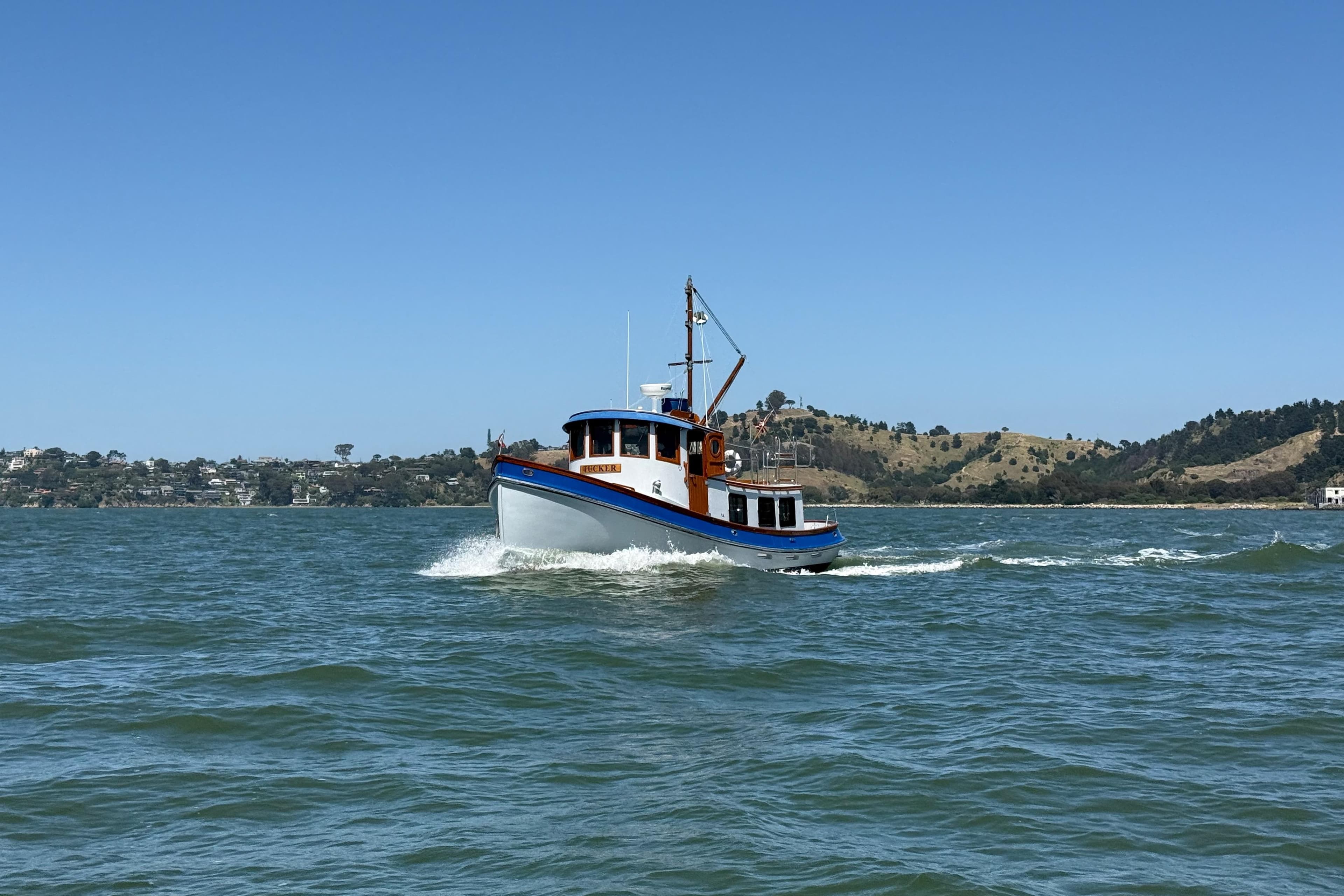 1987 Lord Nelson Victory Tug cruising on a scenic lake under a clear blue sky.