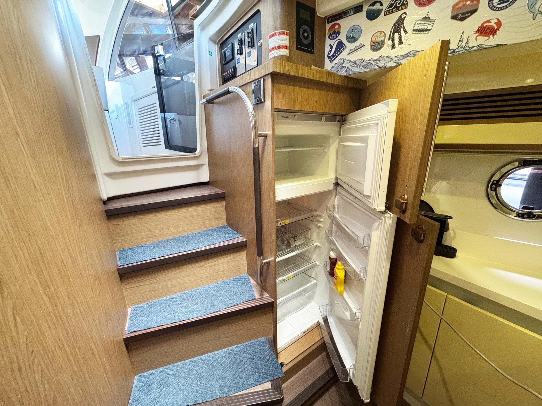 2015 Beneteau Gran Turismo 44 interior with open fridge, wooden stairs, and nautical decor.