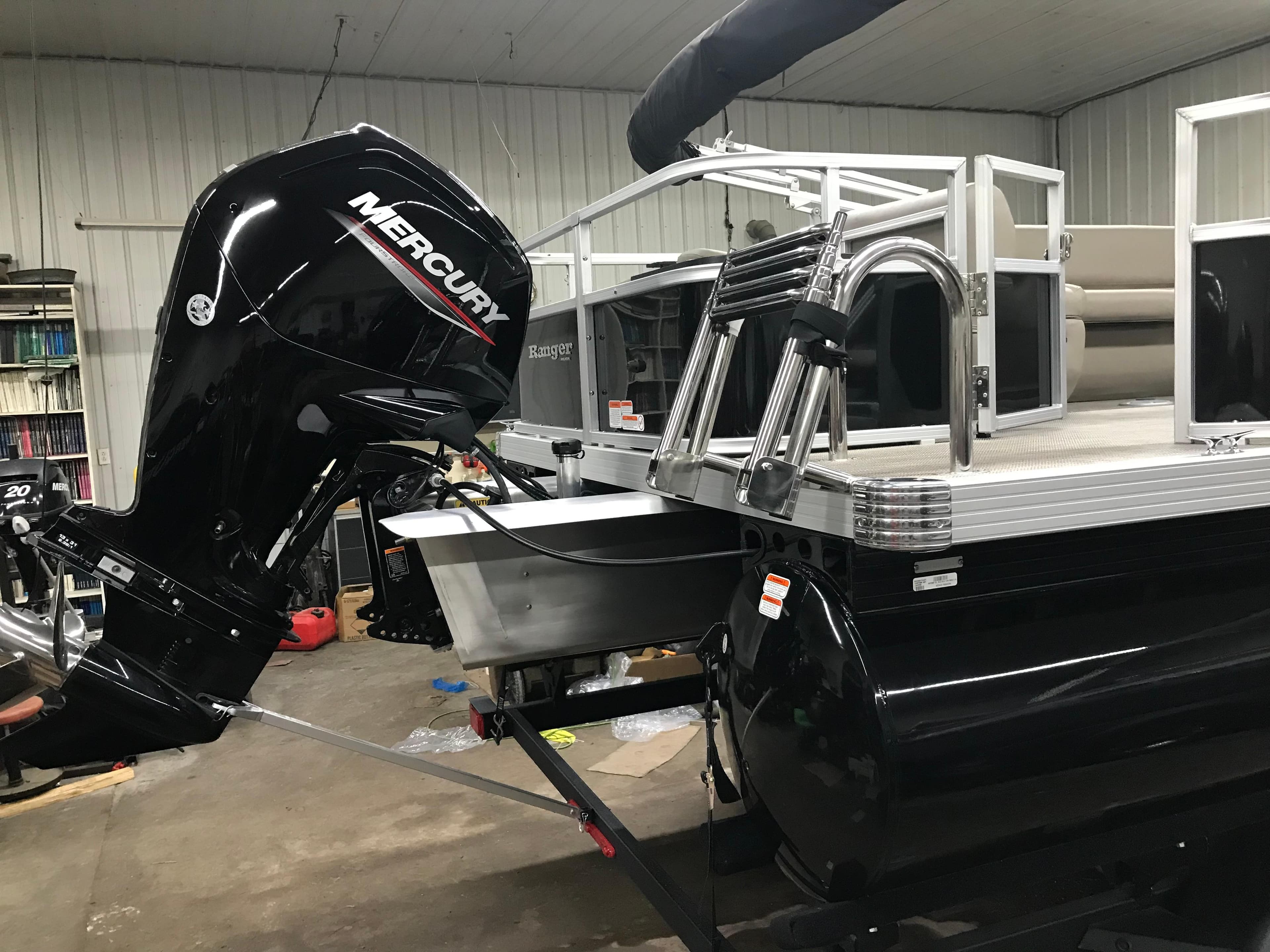2025 Ranger Reata 200F pontoon boat with Mercury outboard motor in a garage.