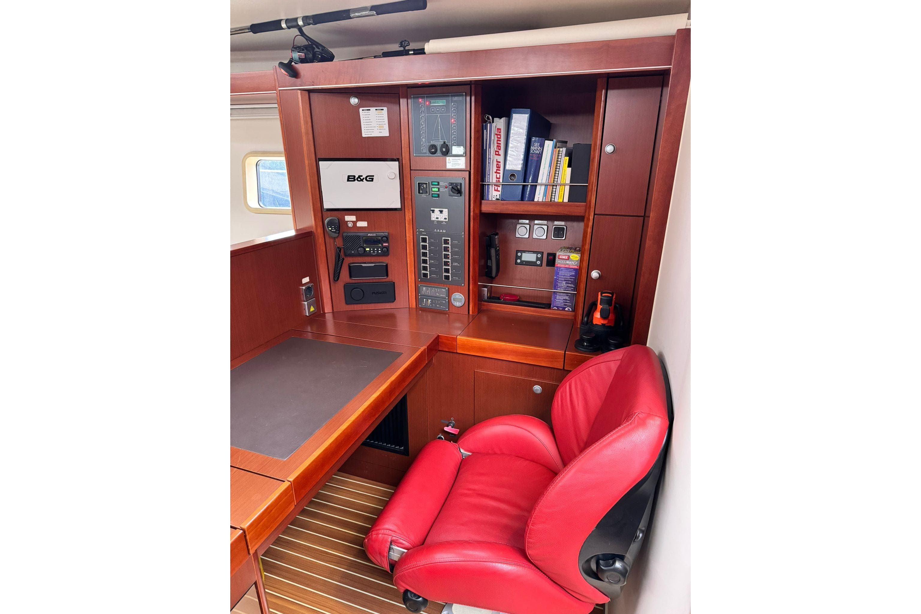 Navigation station with red chair on 2014 Hanse 575 yacht, featuring control panels and storage.