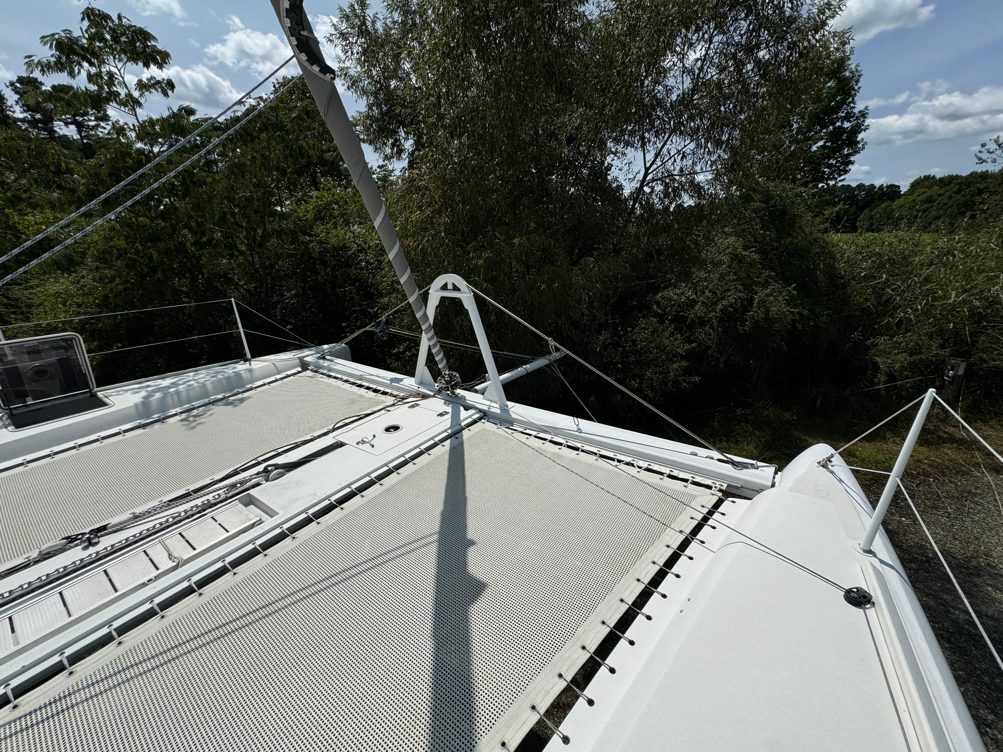 2010 Outremer 49 catamaran deck with netting, surrounded by lush greenery and clear skies.