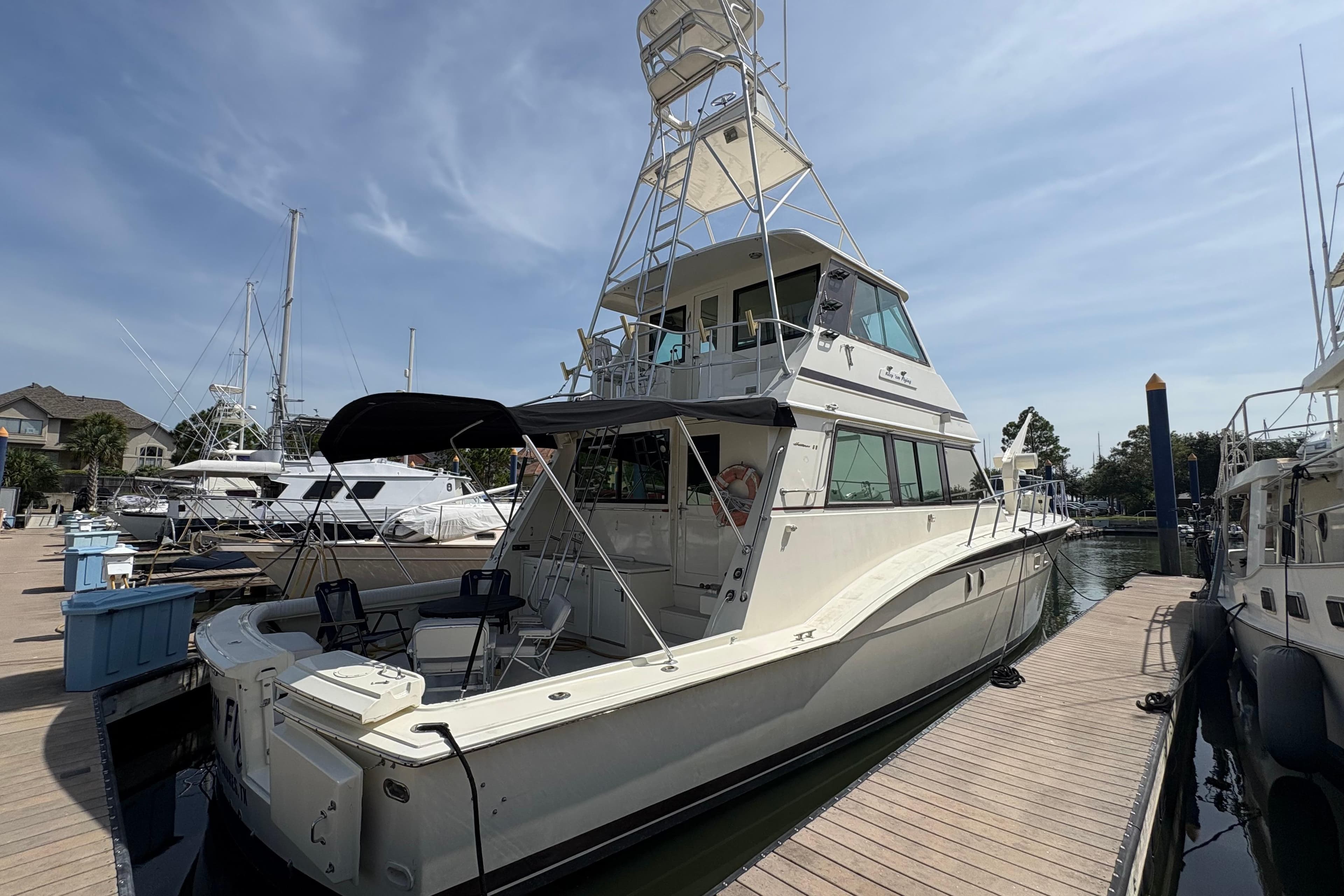 1985 Hatteras 60 Convertible yacht docked at marina under clear sky.