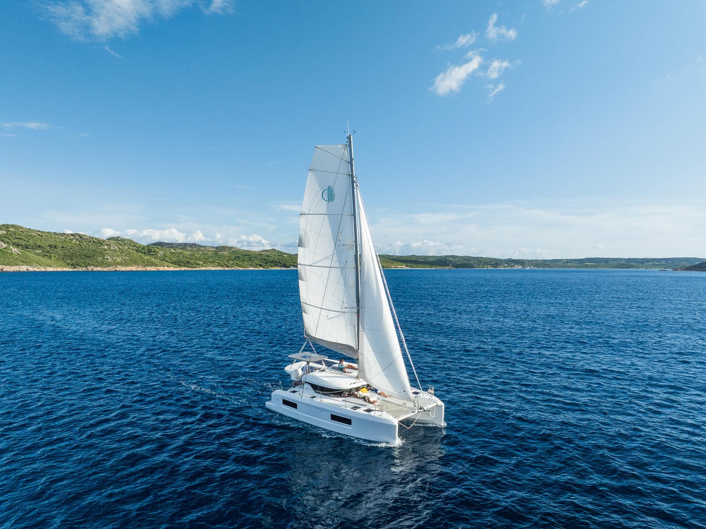 Sailing catamaran Lagoon 38, 2025 model, cruising on blue ocean under clear sky.