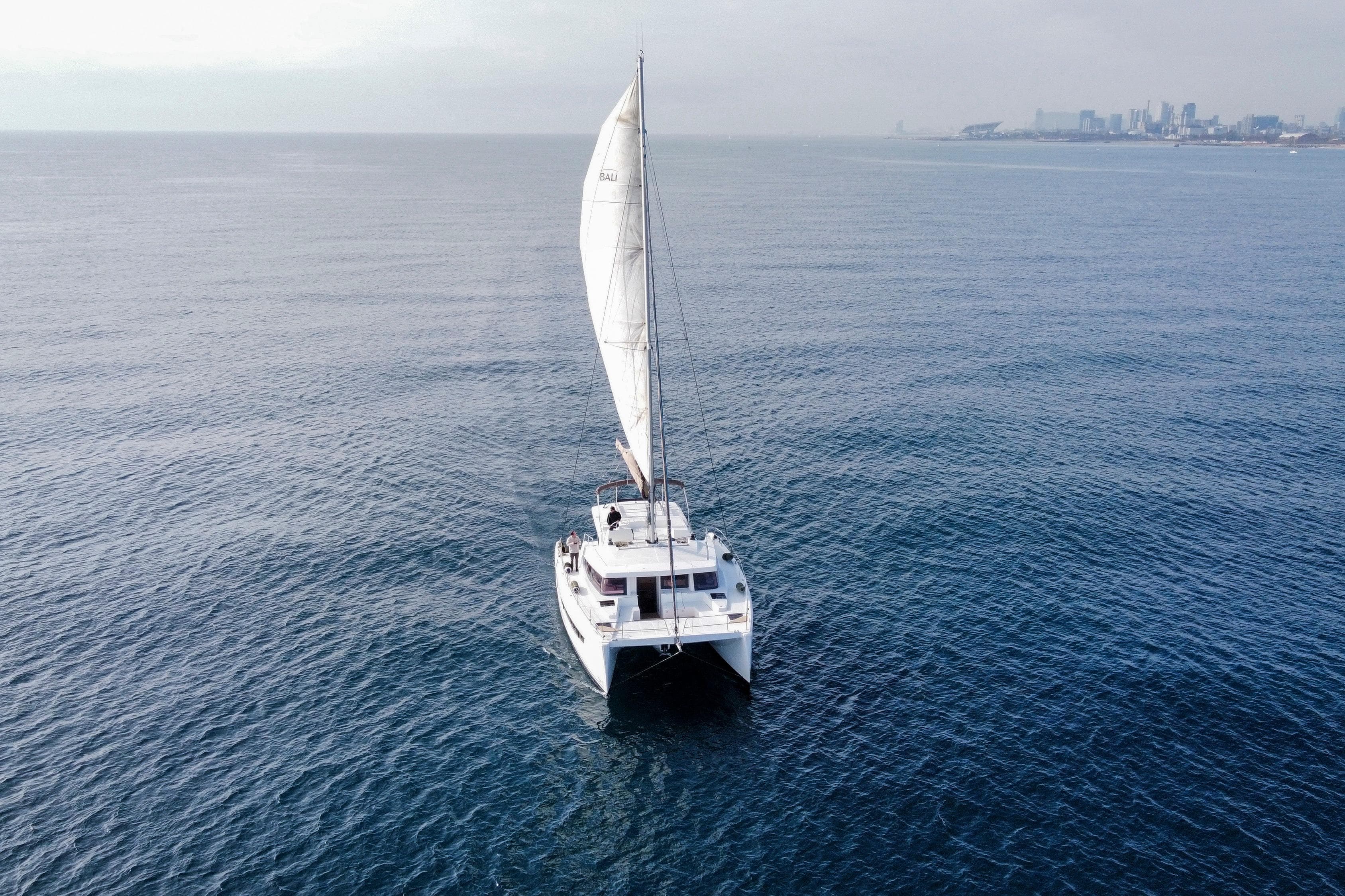 Sailing catamaran Bali 4.8, 2020 model, cruising on open sea with city skyline.