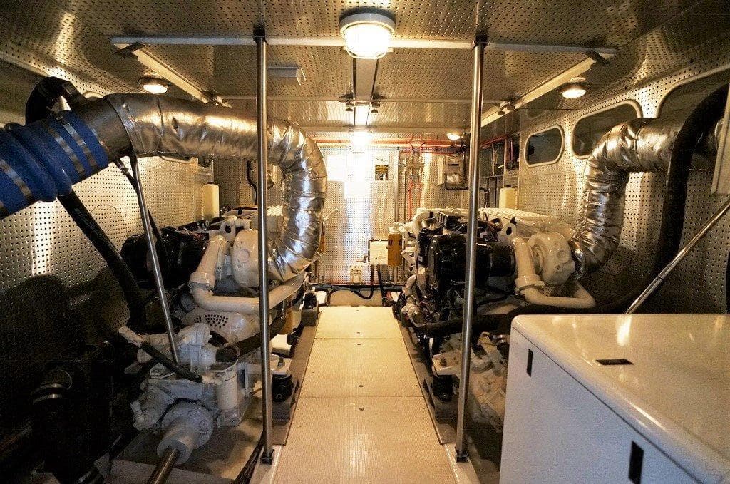Engine room of 2027 Legend Boats 630 Flybridge, featuring dual engines and metallic piping.