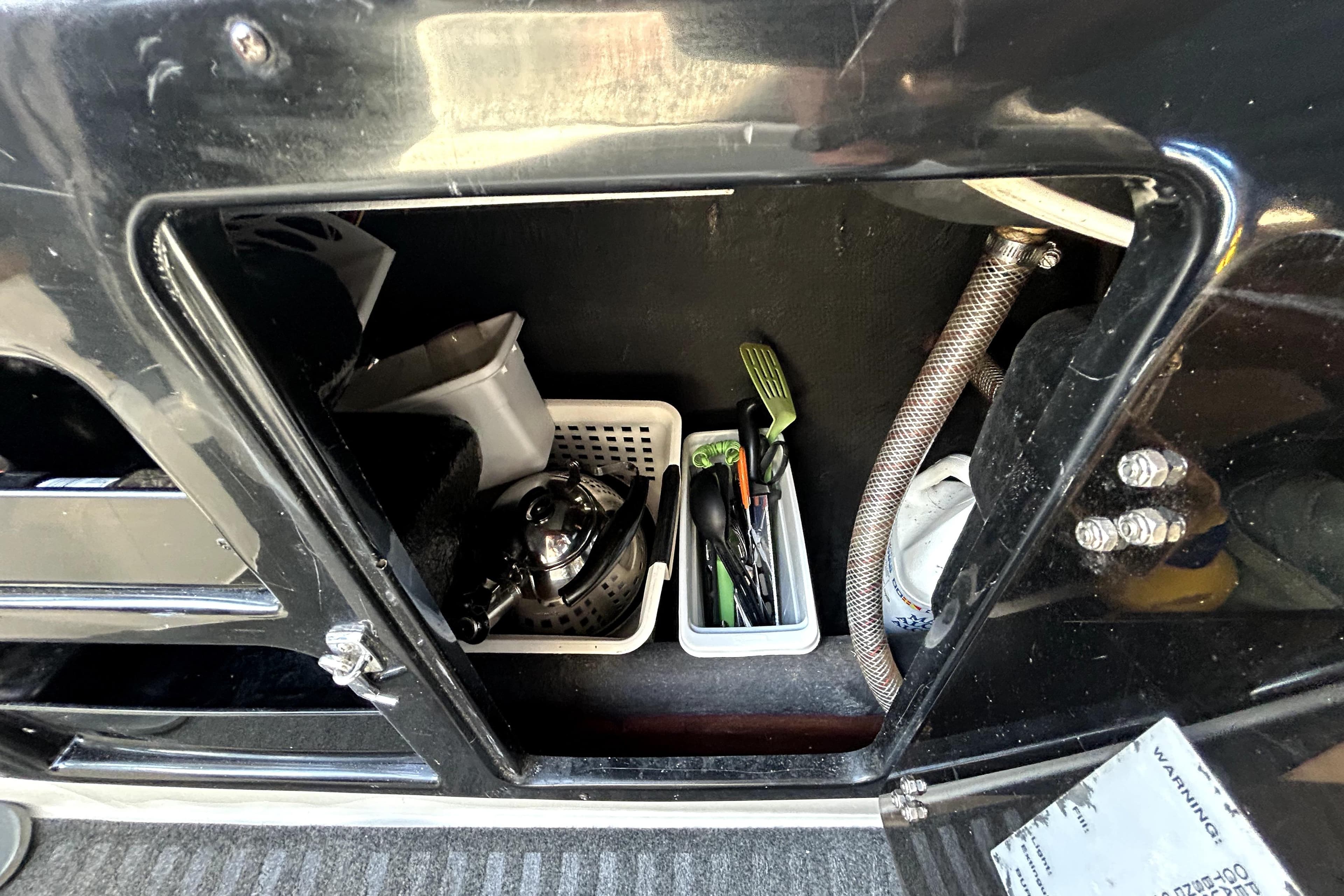 Storage compartment in a 1998 MacGregor 26X Powersailer with kitchen utensils and kettle.