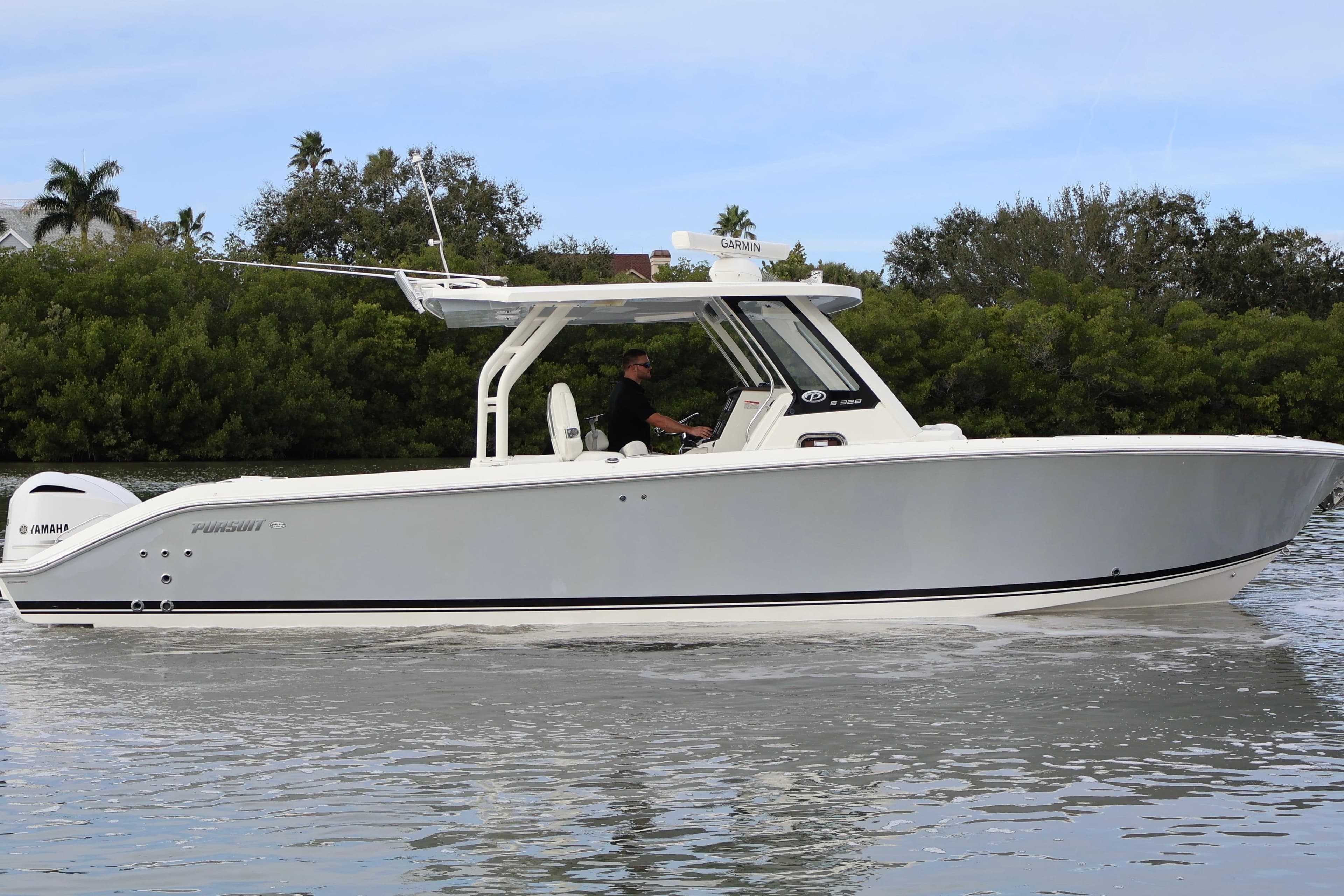 2021 Pursuit S 328 Sport boat cruising on calm water, surrounded by lush greenery.