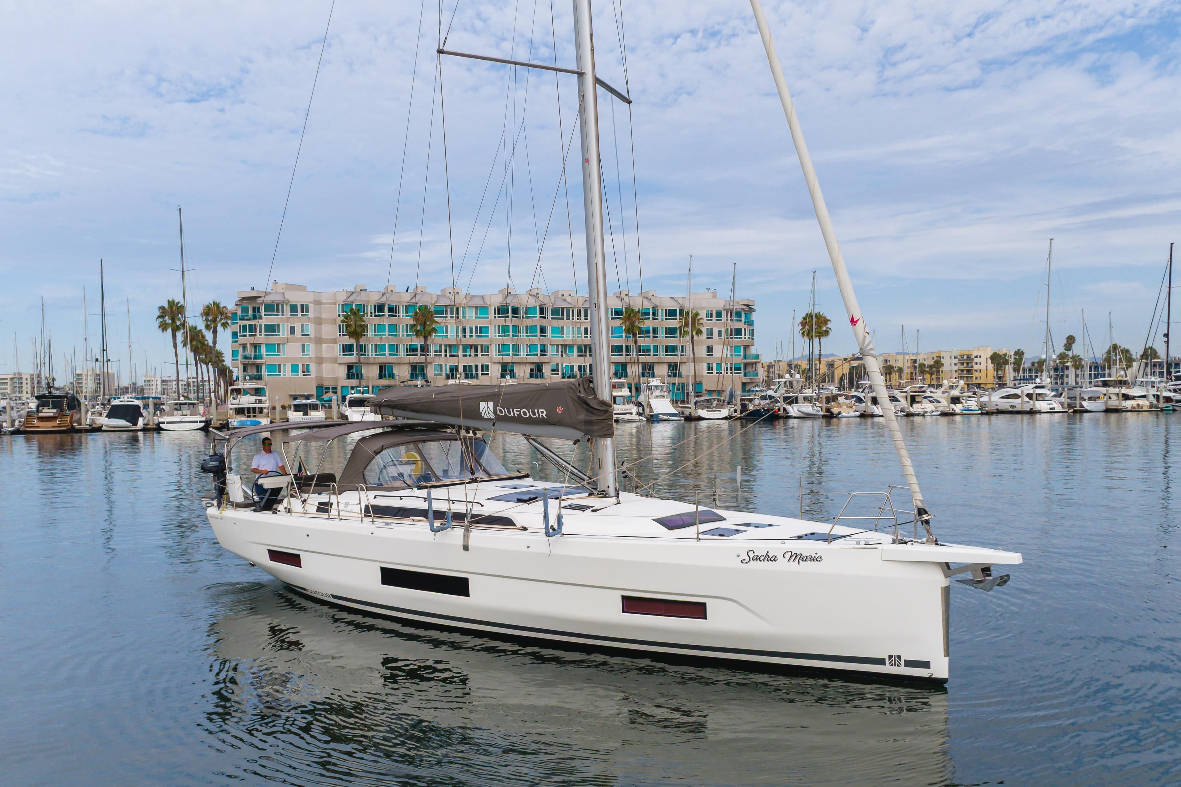 2024 Dufour 470 sailboat docked in marina, modern design, calm waters, coastal backdrop.