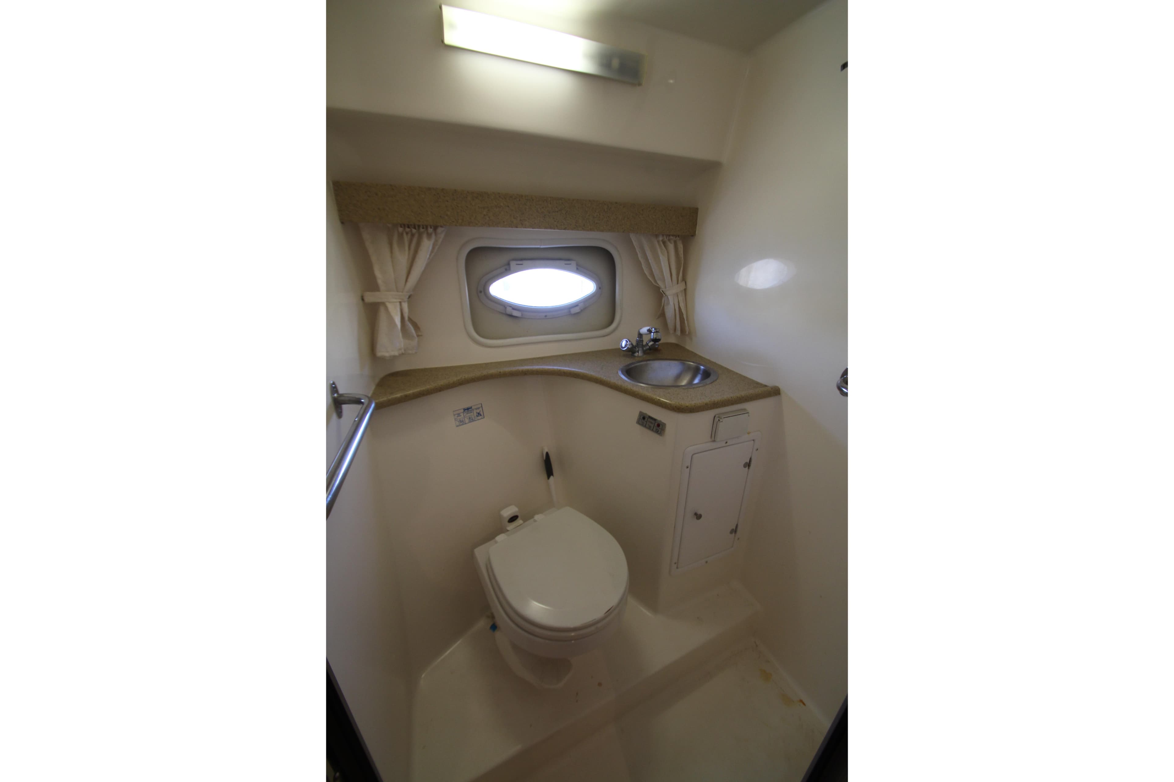 2006 Rinker 320 Express Cruiser bathroom with toilet, sink, and porthole window.