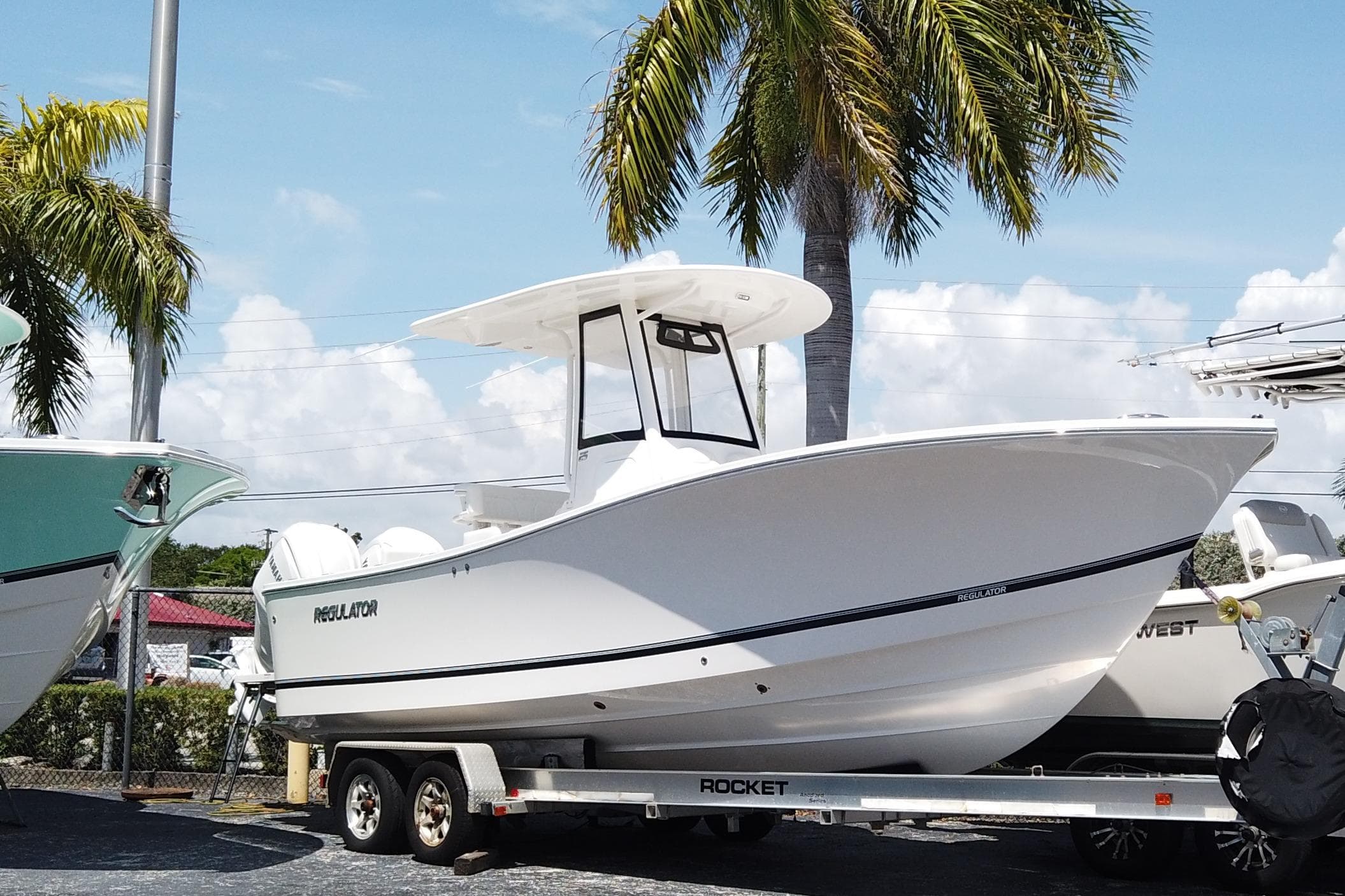 2025 Regulator 25 boat on trailer, parked under palm trees, clear sky background.
