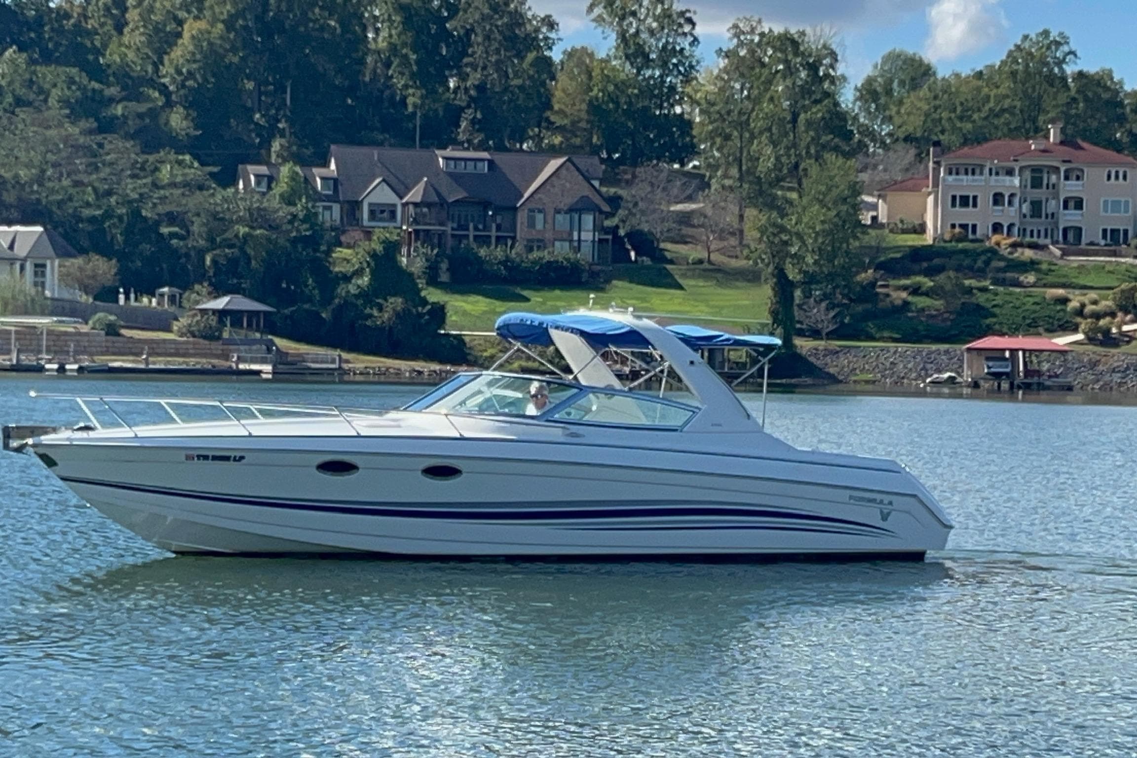 2004 Formula 330 Sun Sport boat cruising on a scenic lake with waterfront homes.