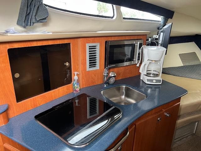2006 Bayliner 275 boat interior kitchen with sink, stove, microwave, and coffee maker.