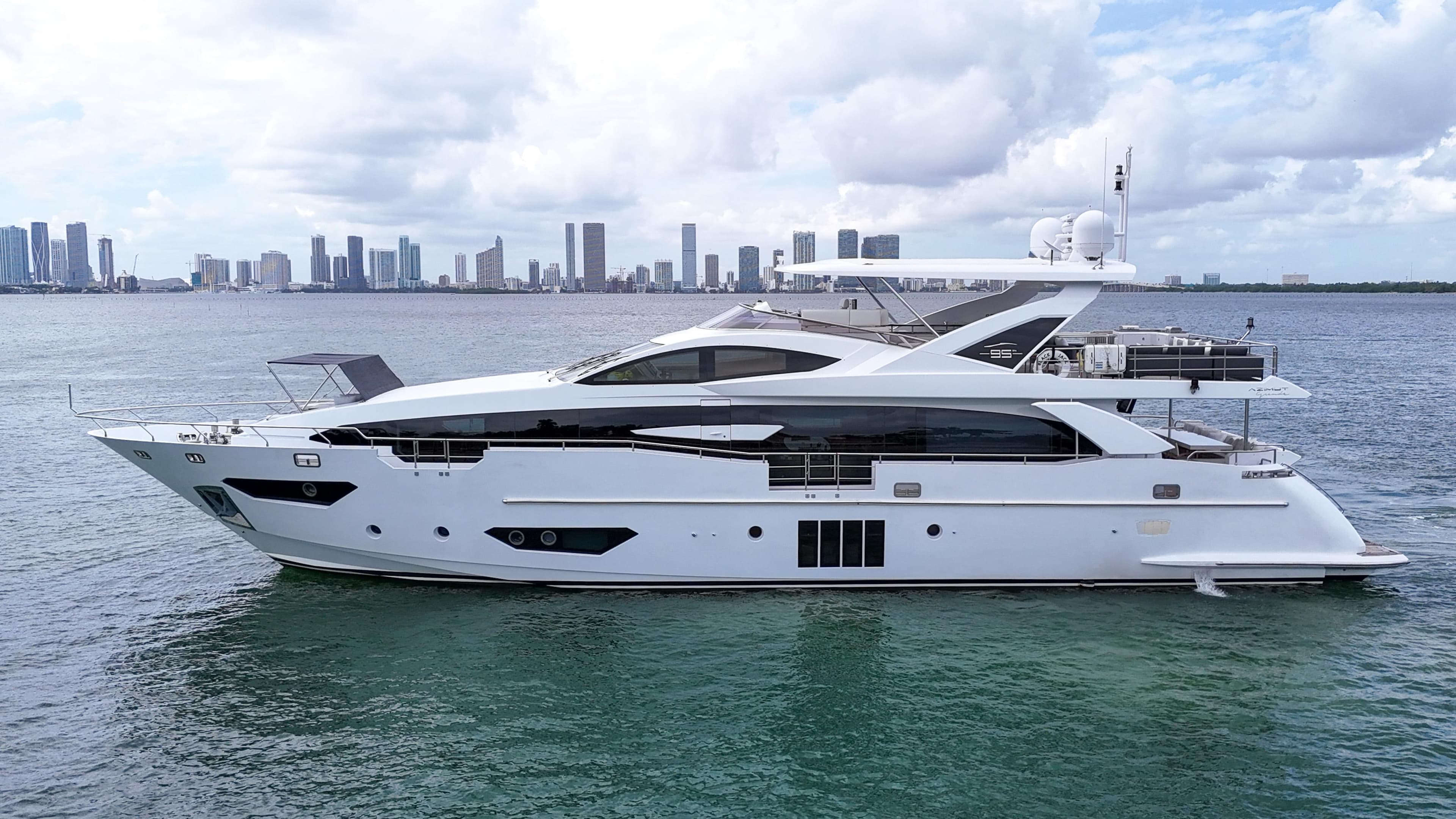 Luxury 2017 Azimut 95 Raised Pilothouse yacht on calm water with city skyline.