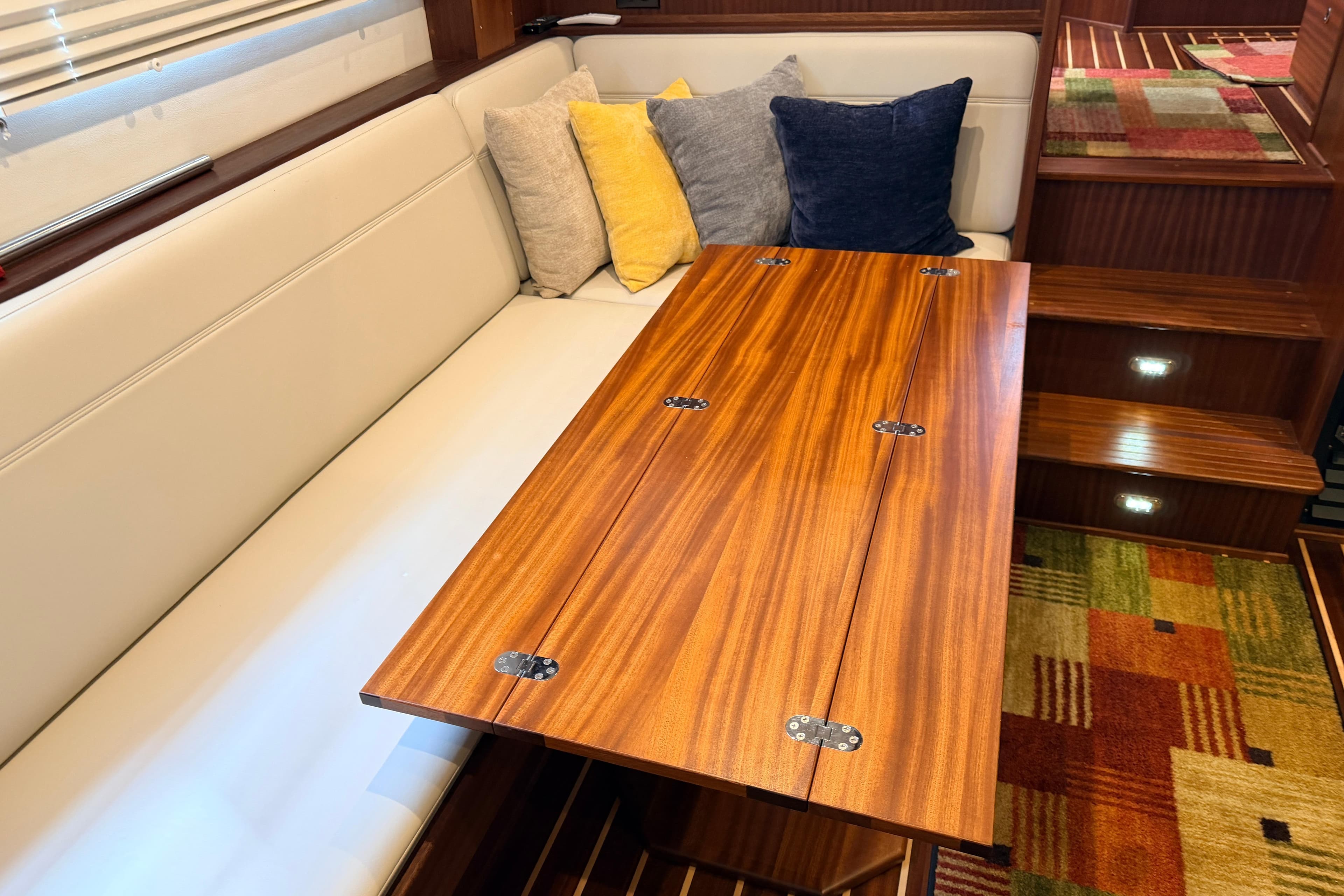 Interior of 2022 American Tug 365 with wooden table, cushioned seating, and colorful pillows.
