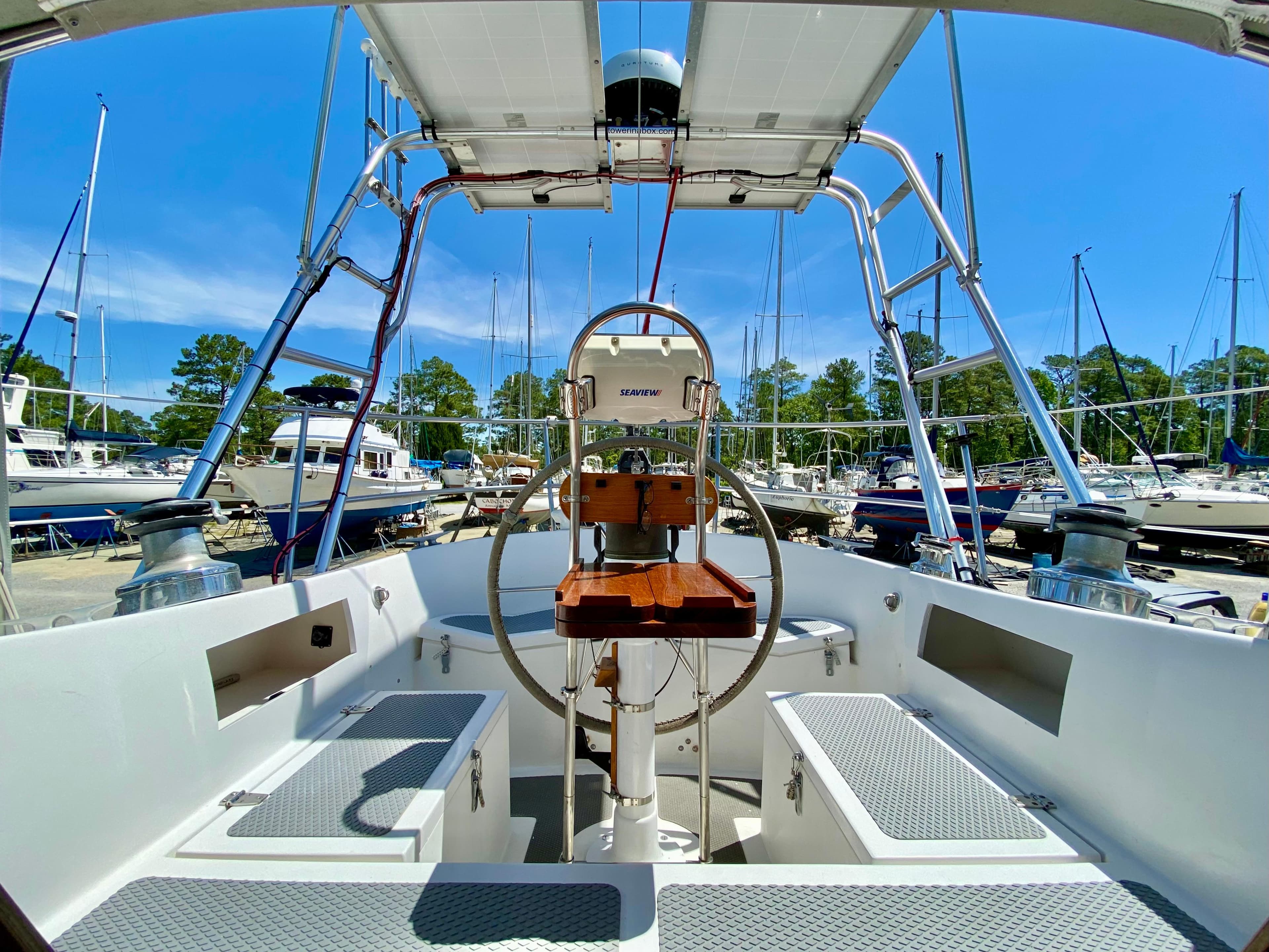 1979 Valiant 37 sailboat cockpit with steering wheel, docked in a marina under clear blue sky.