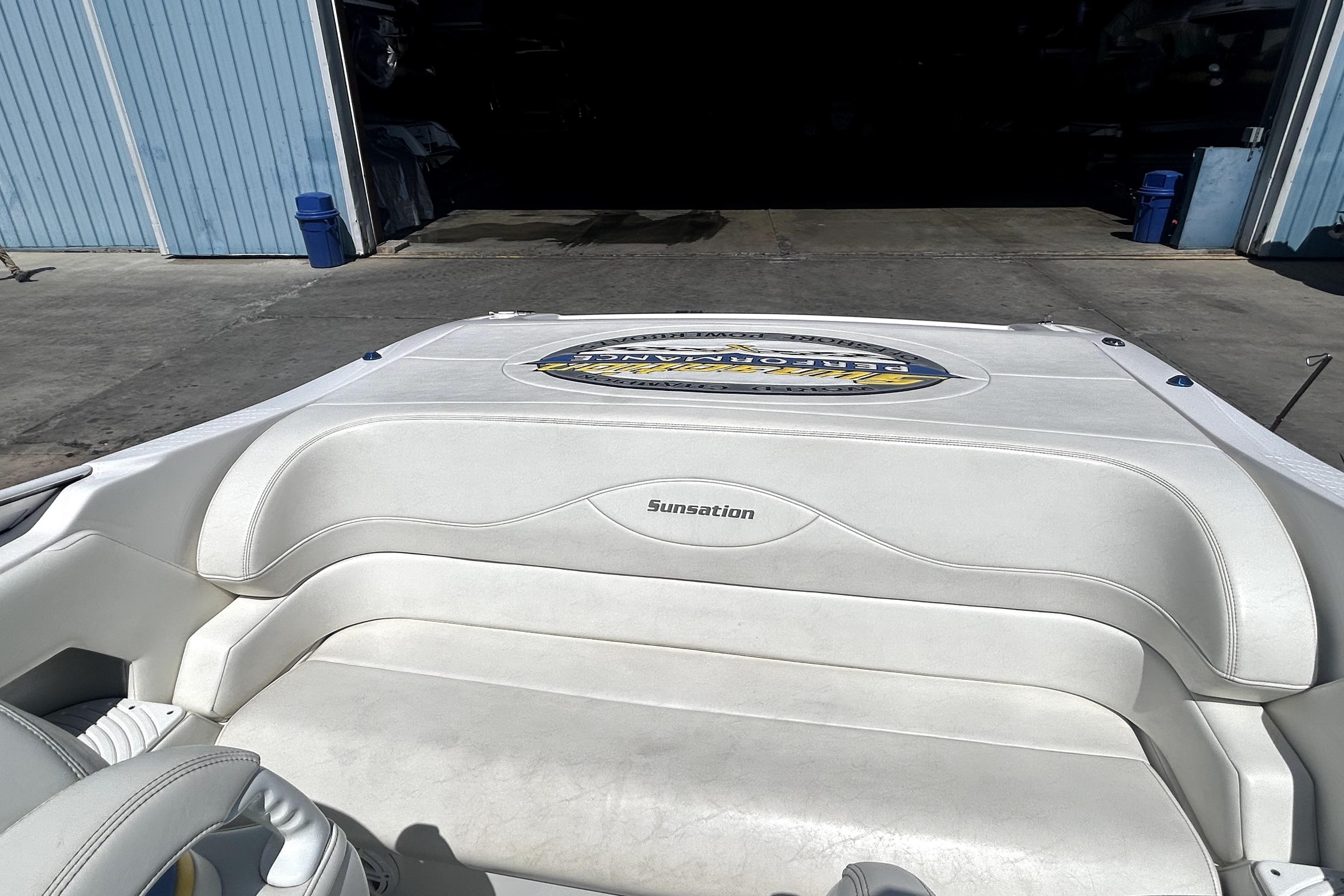 2007 Sunsation 32 Dominator boat with white seating, docked near a blue building.