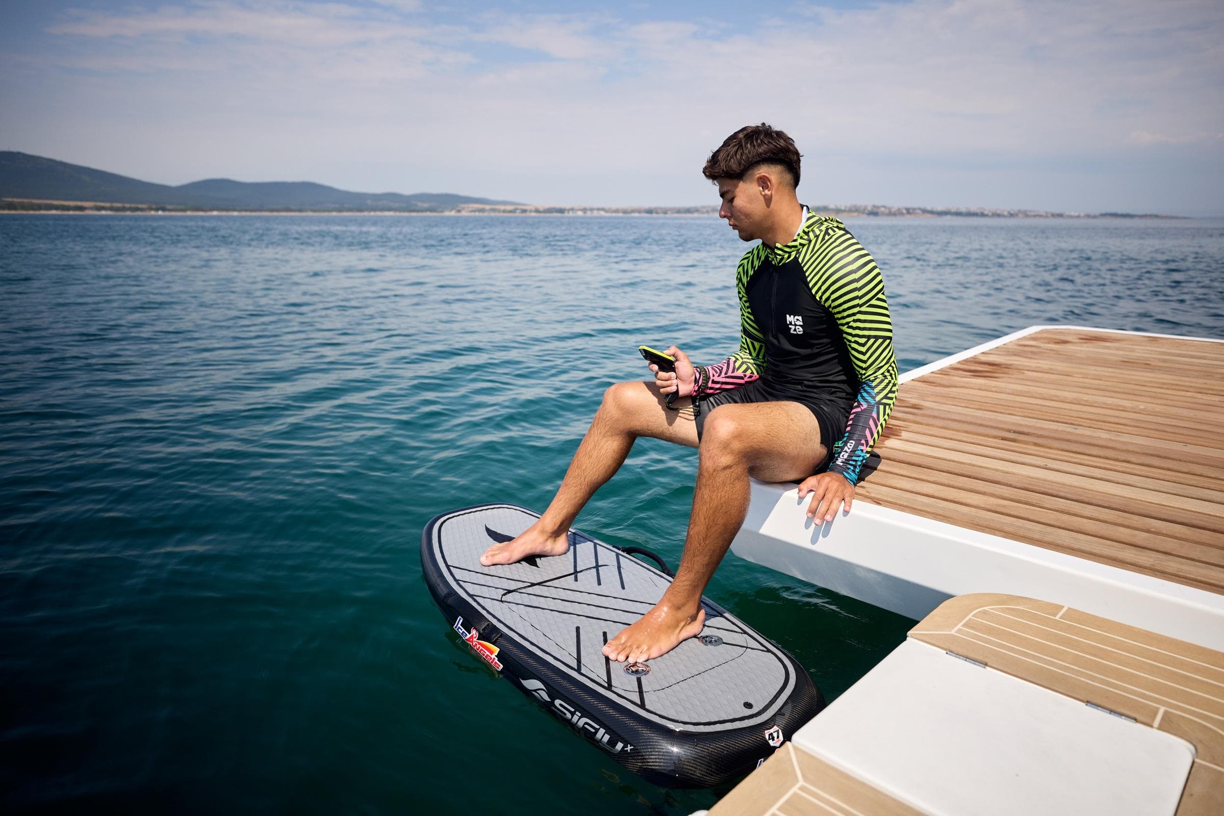 Man sitting on Omaya 50 Power Catamaran, holding phone, with scenic ocean view.