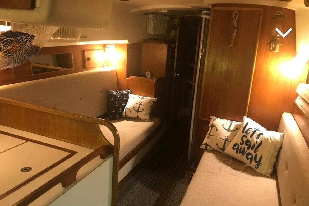 Cozy interior of 1980 Pearson 365 Sloop with nautical-themed cushions and warm lighting.
