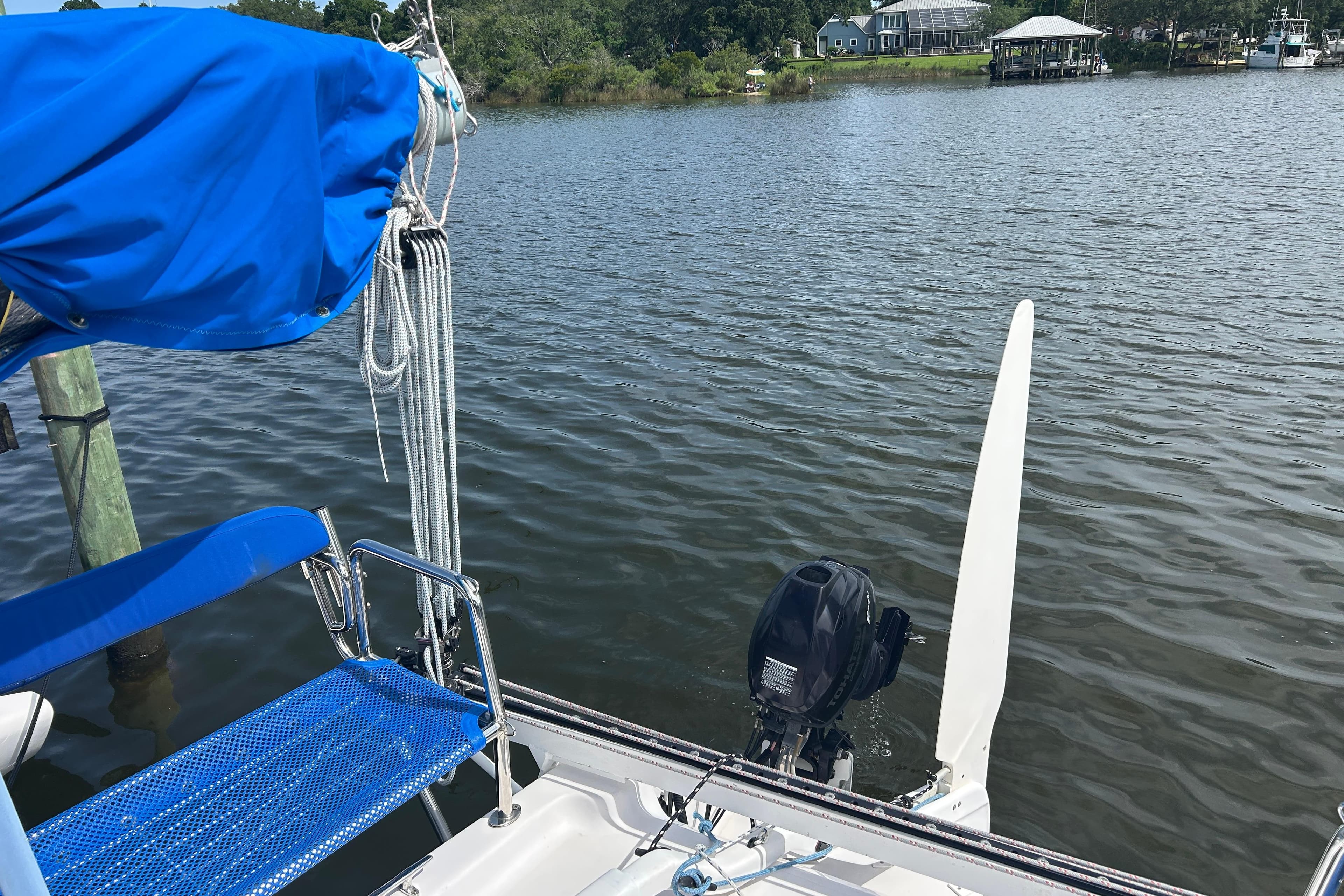 Sailboat Corsair 970 (2017) docked by a serene lake with blue cover and motor.