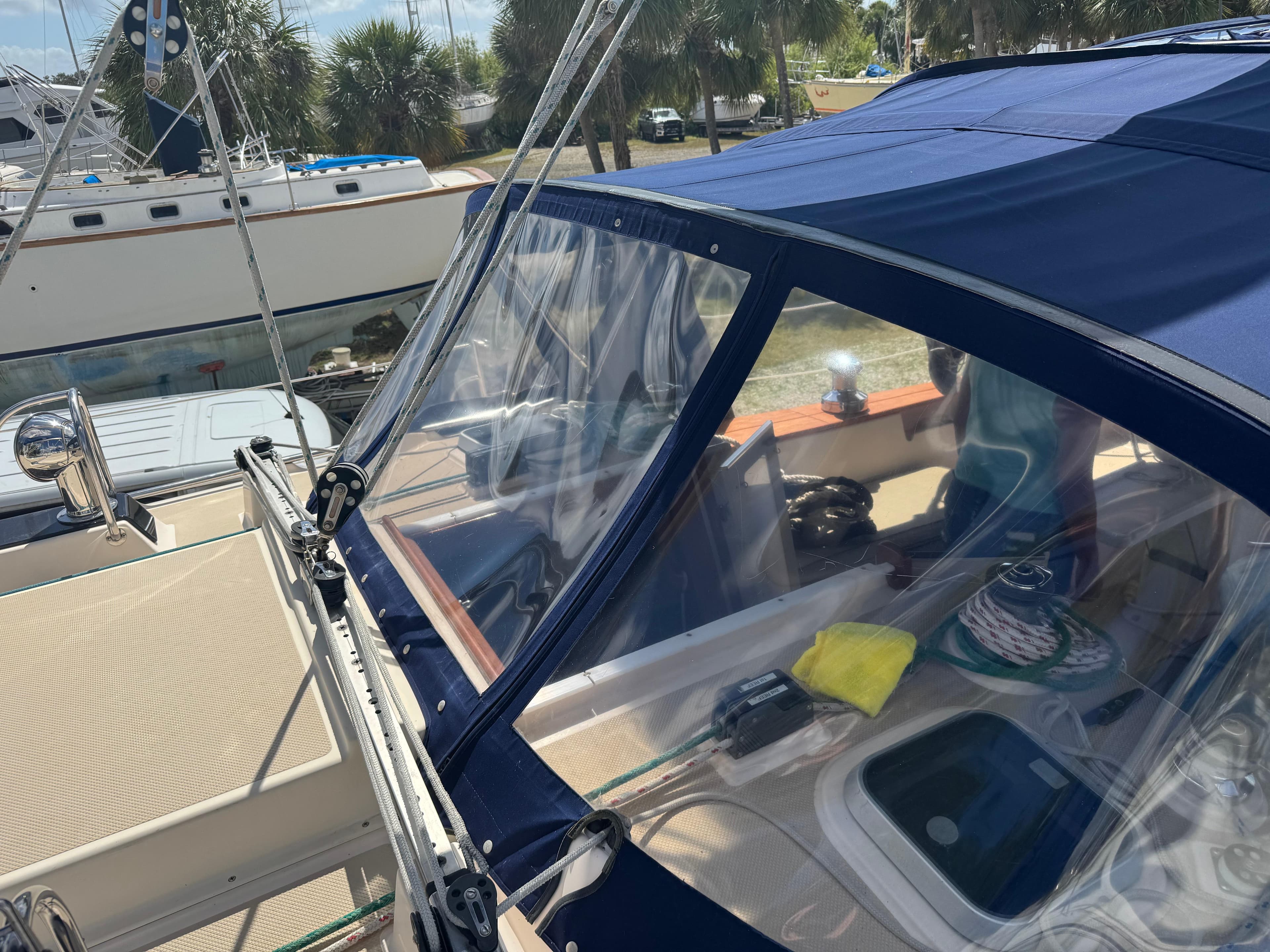 2002 Island Packet 380 sailboat cockpit with blue canopy and clear windows, docked near palm trees.