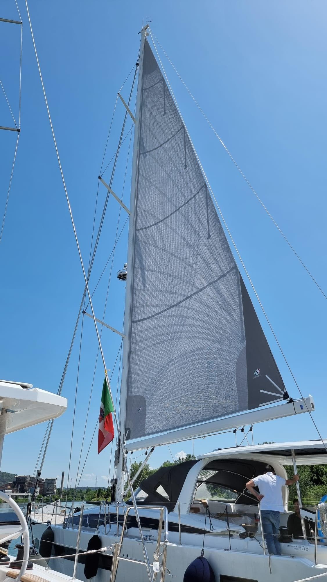 2023 Jeanneau 65 sailboat with raised sails under clear blue sky.