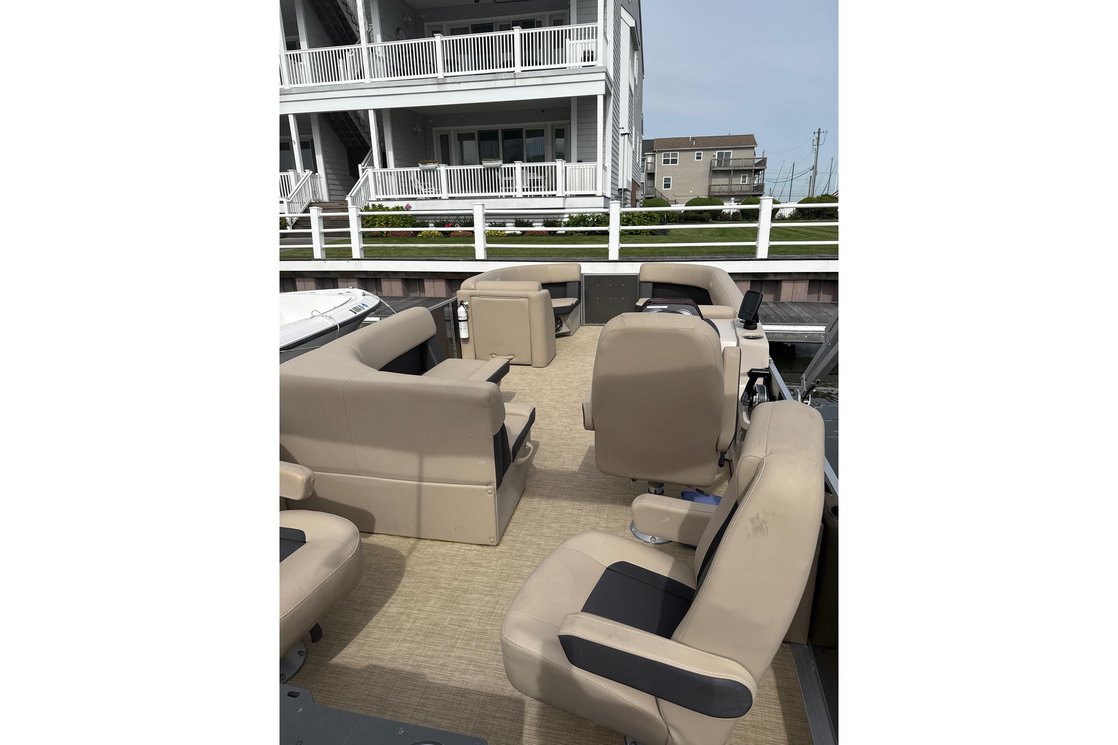 2025 Harris Cruiser 230 pontoon boat with beige seating, docked near waterfront homes.