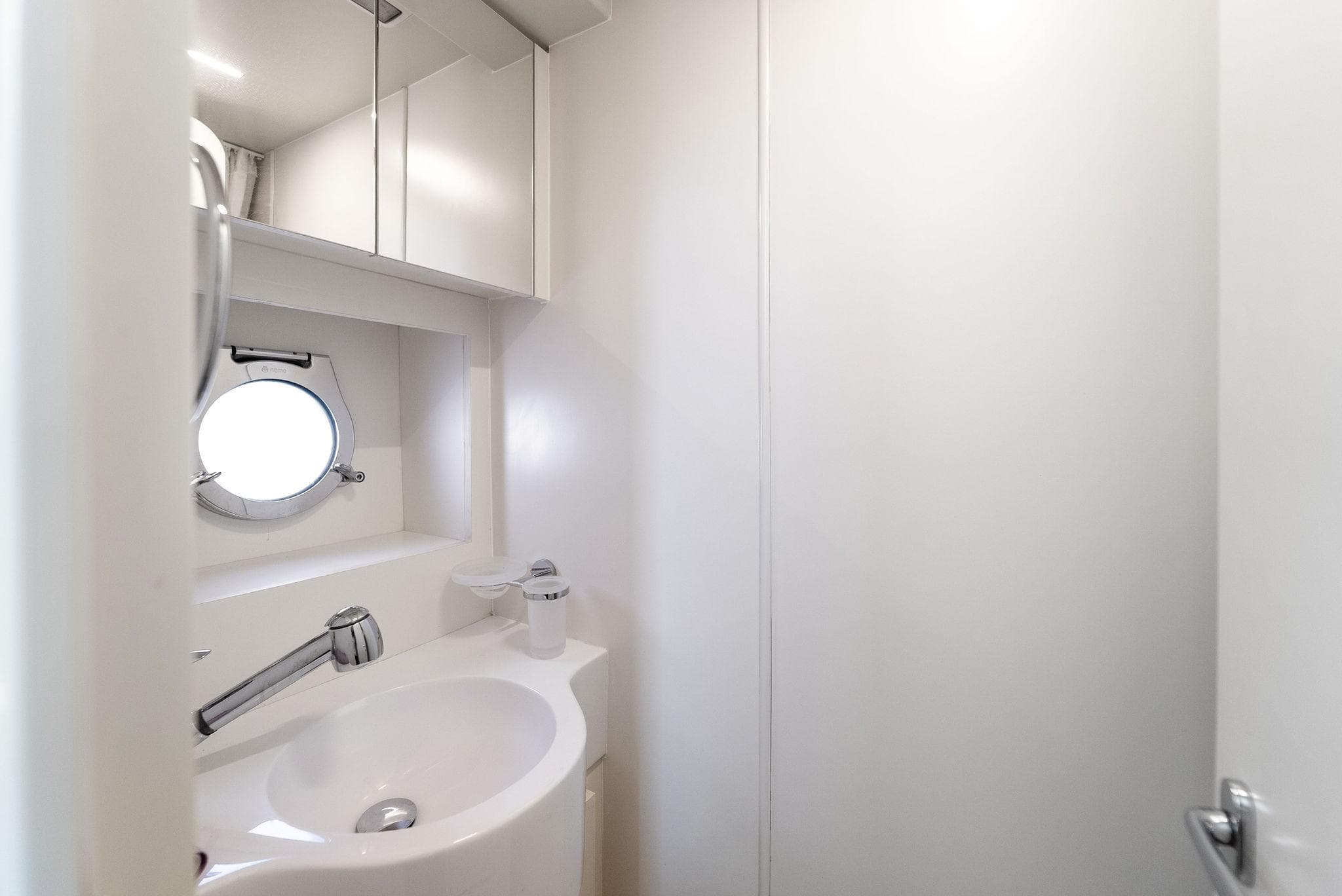 Modern bathroom interior on 2023 Ferretti Yachts 670, featuring sleek white design and round porthole window.