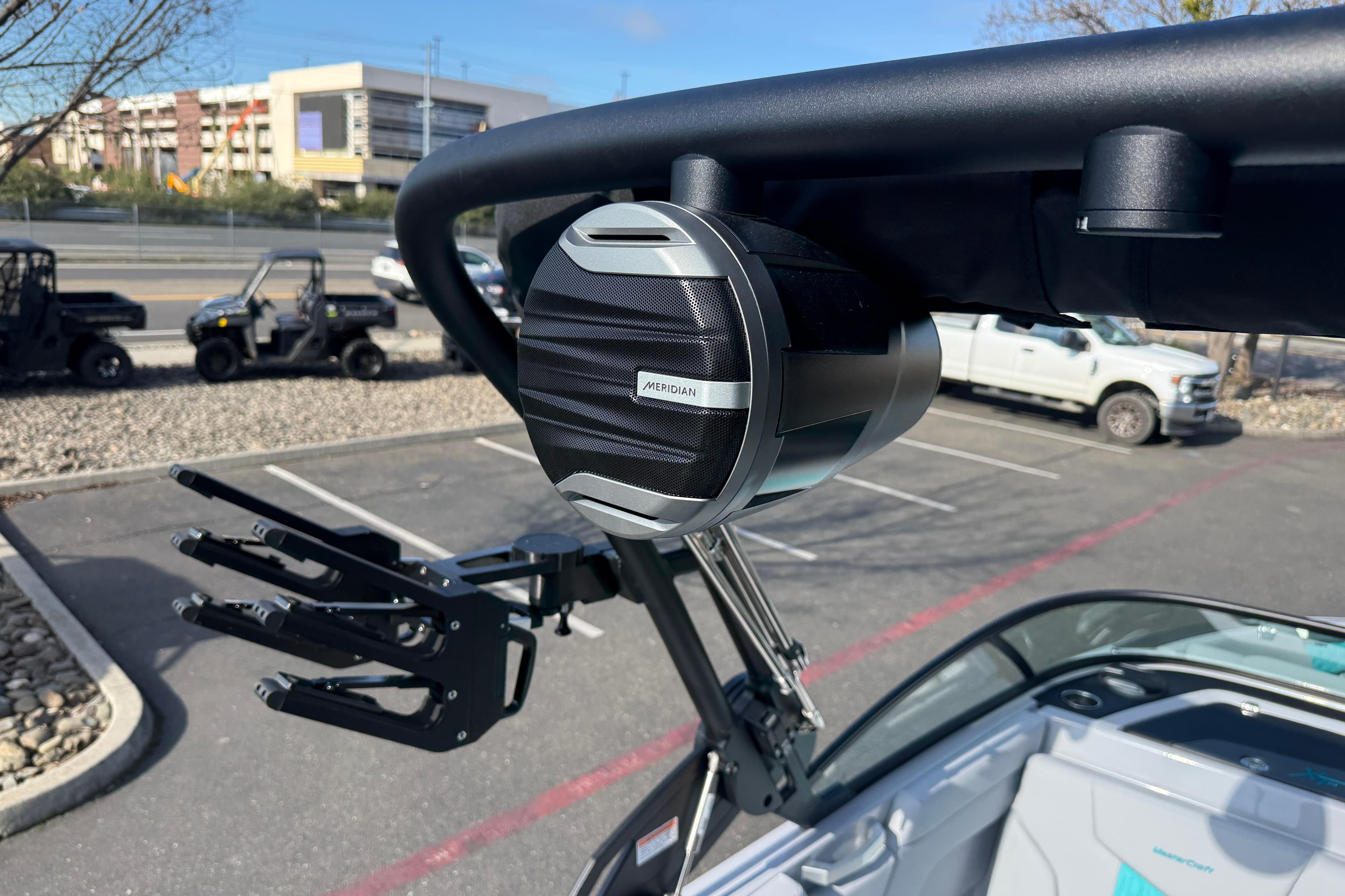 2026 MasterCraft XT23 boat with mounted speaker and wakeboard rack in a parking lot.
