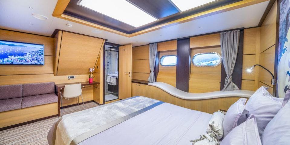 Luxurious yacht bedroom with modern decor, featuring a double bed, porthole windows, and a seating area.