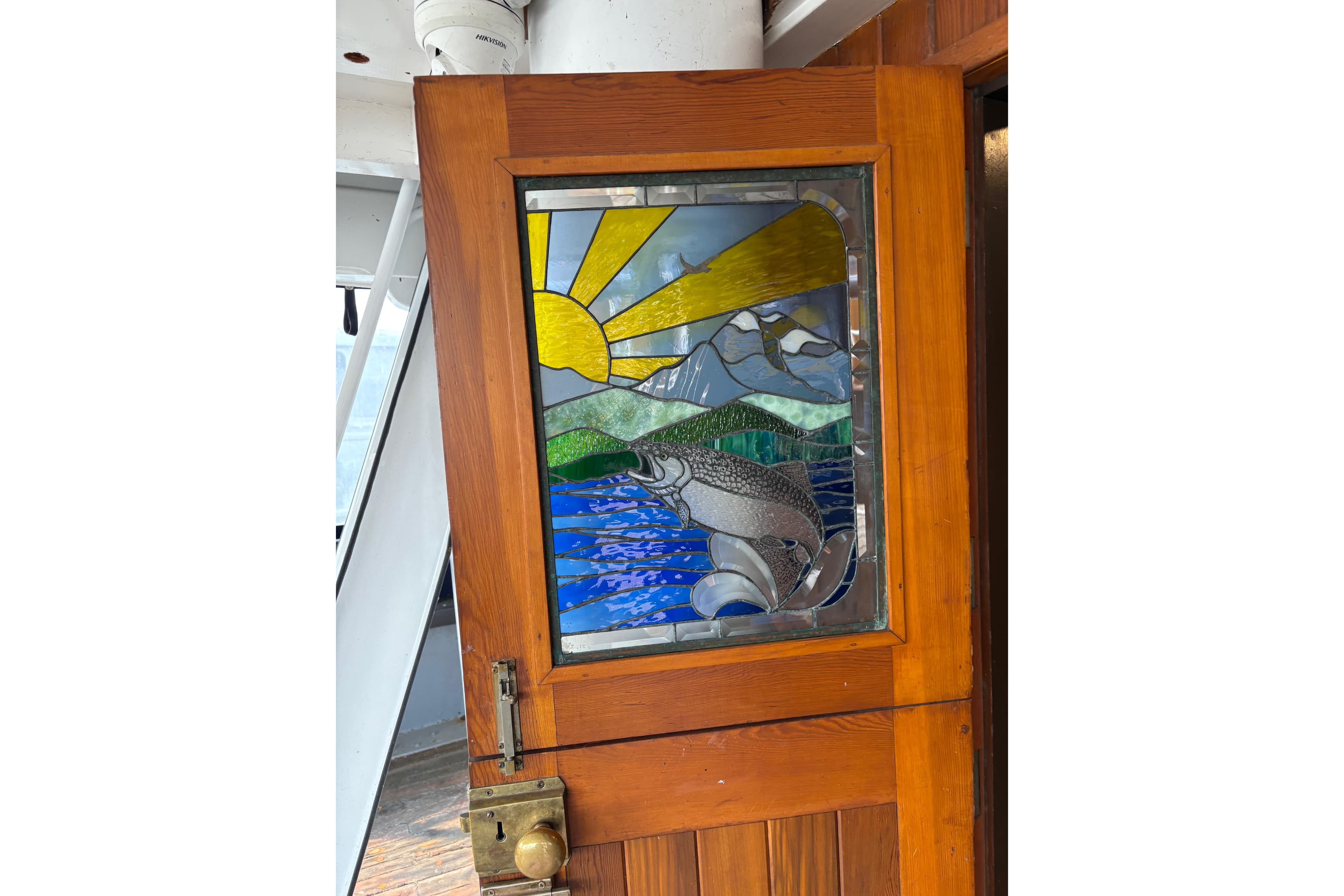 Stained glass door on 1941 McKenzie Tug, featuring sun, mountains, and fish design.
