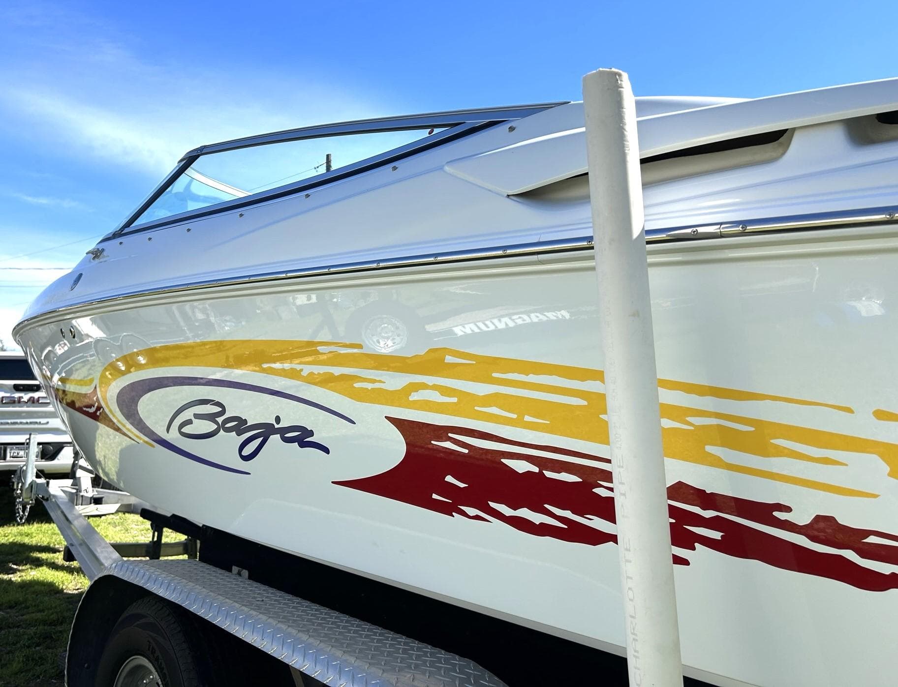 2002 Baja 232 boat with colorful graphics on a trailer under a clear blue sky.