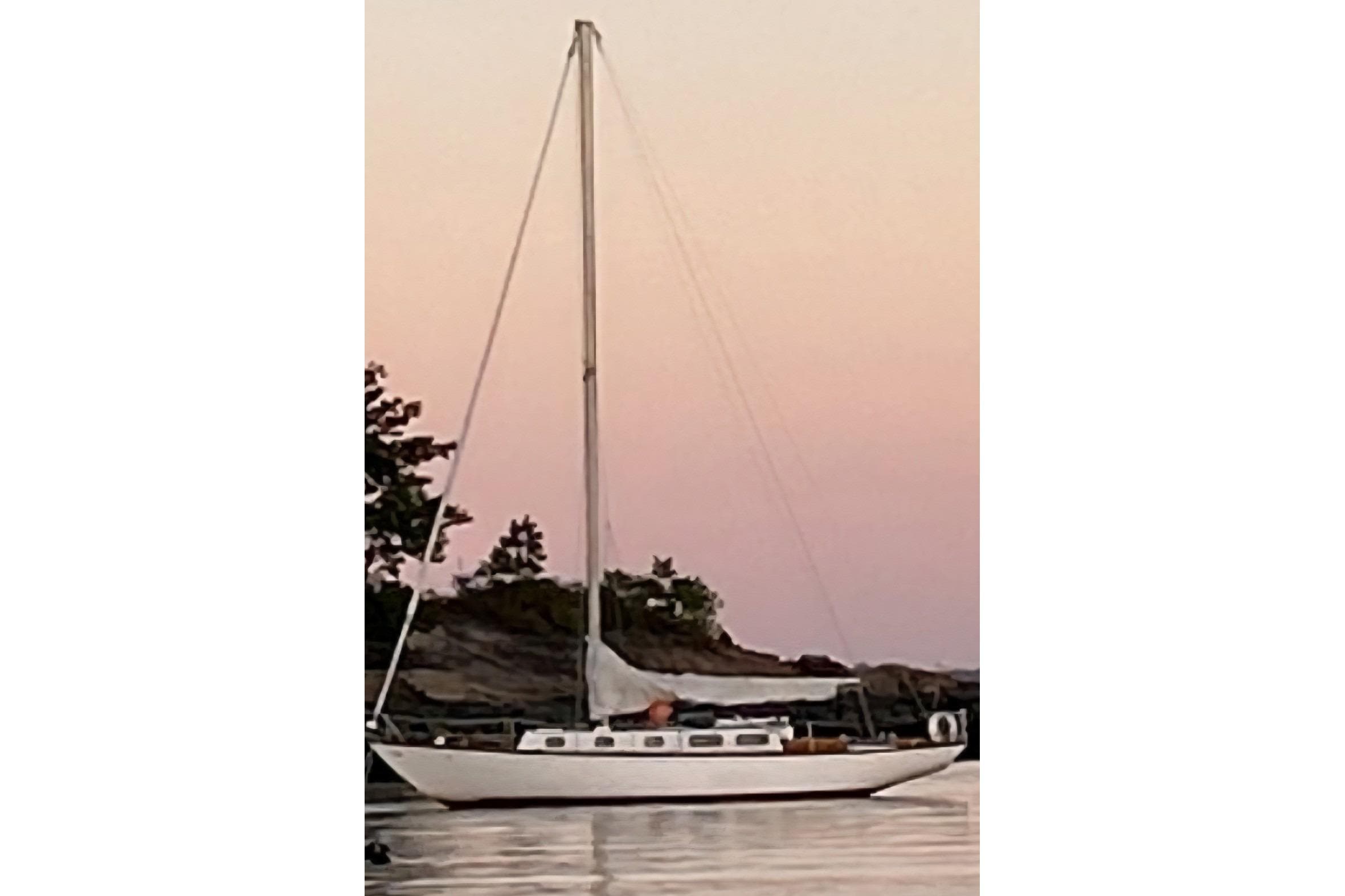 Vintage 1969 Tartan 37 sailboat at sunset, anchored near rocky shoreline.